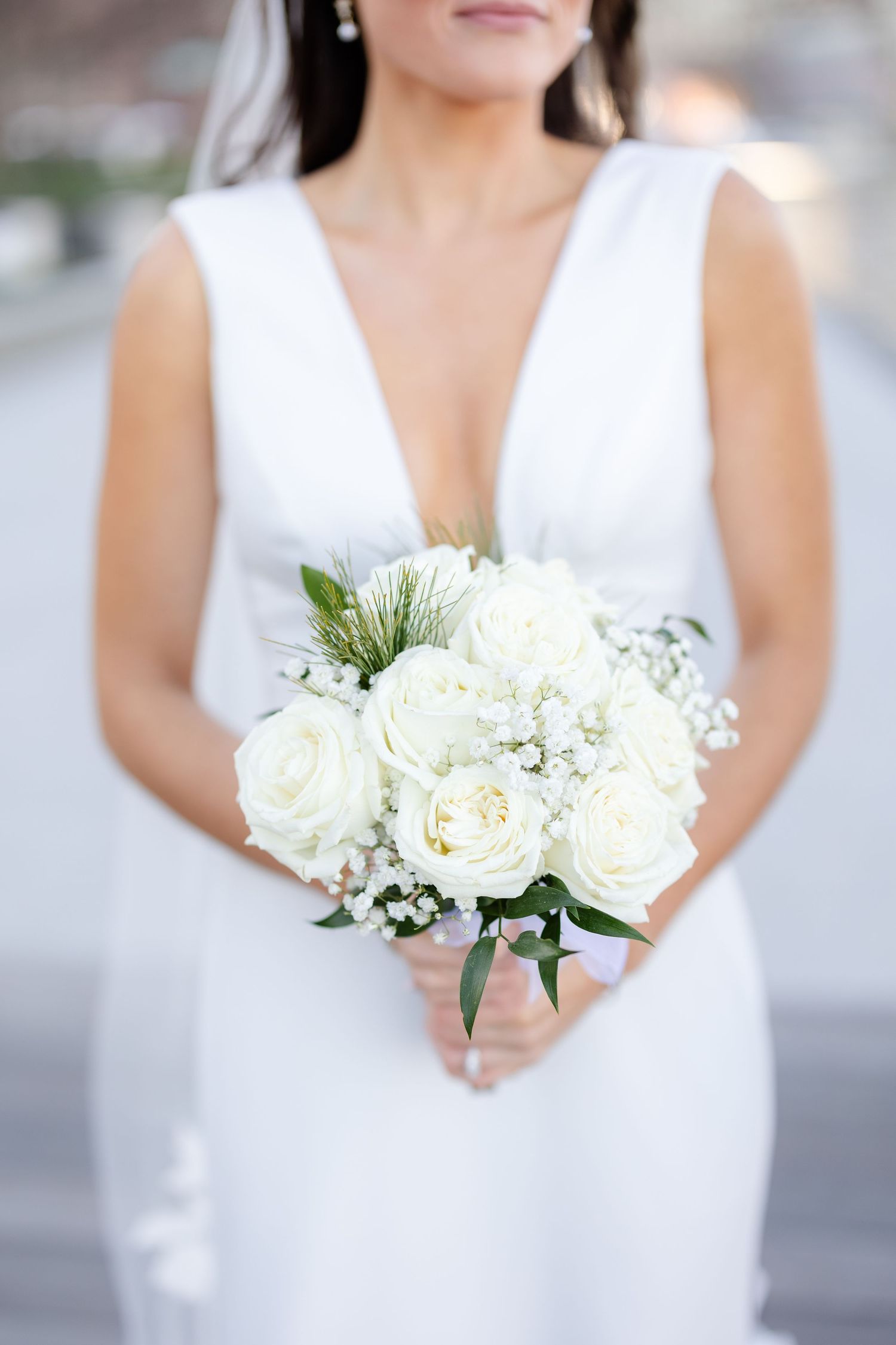 Bride in deep V-neck white gown holding classic white rose and baby's breath bouquet.