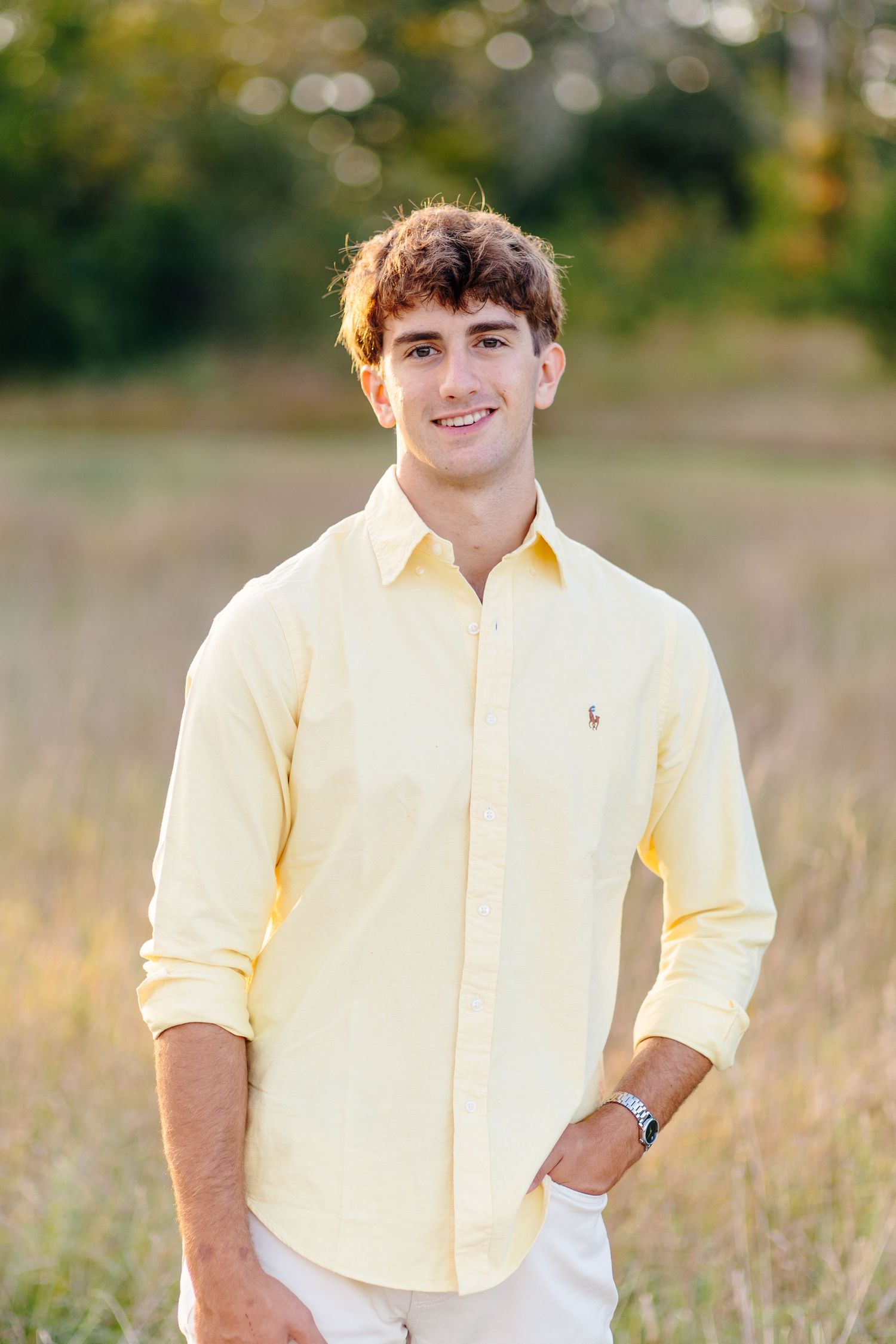 Young man in yellow Ralph Lauren shirt smiling in sunny field.