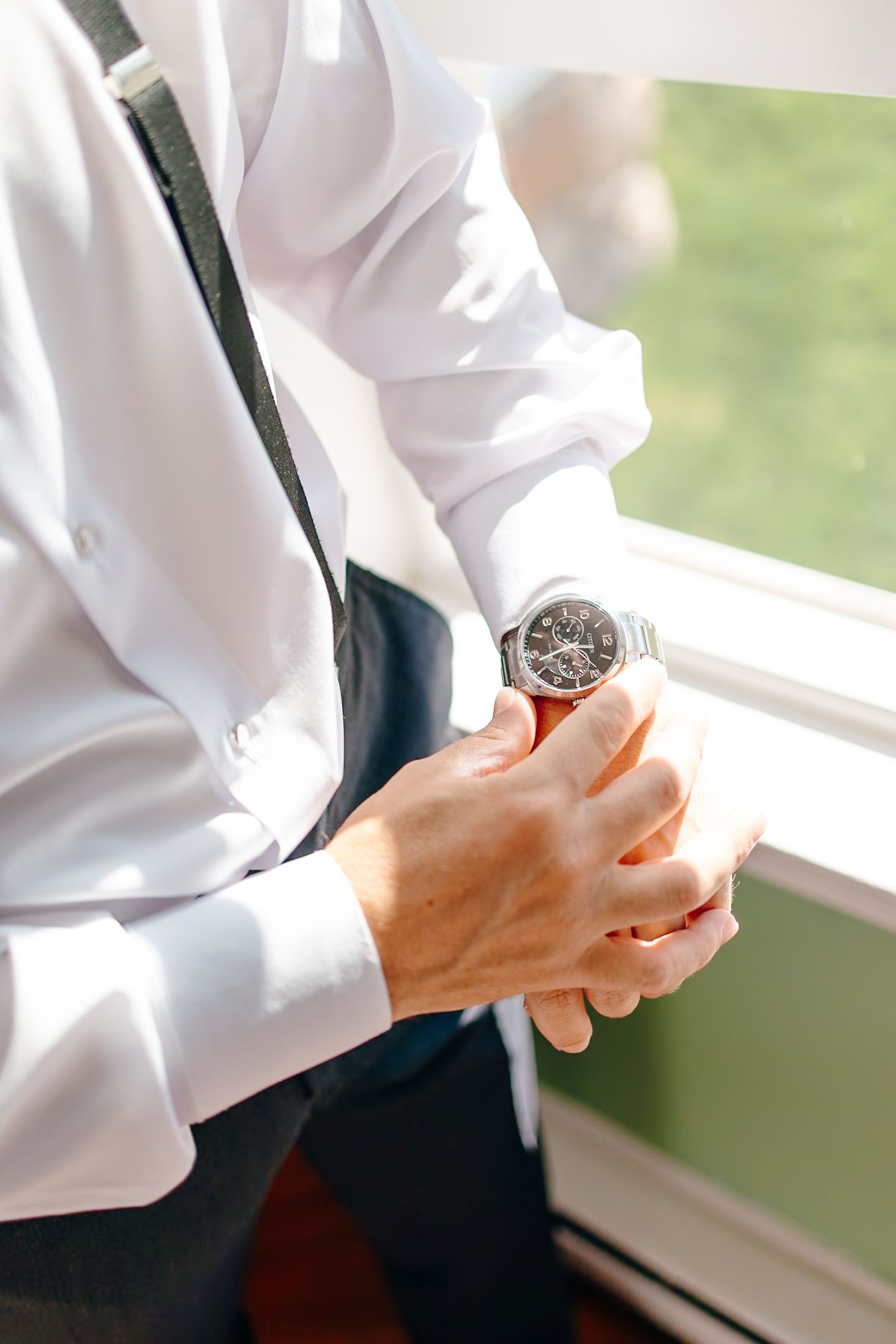 Man in white shirt and suspenders checking his wristwatch, elegant groom getting ready.