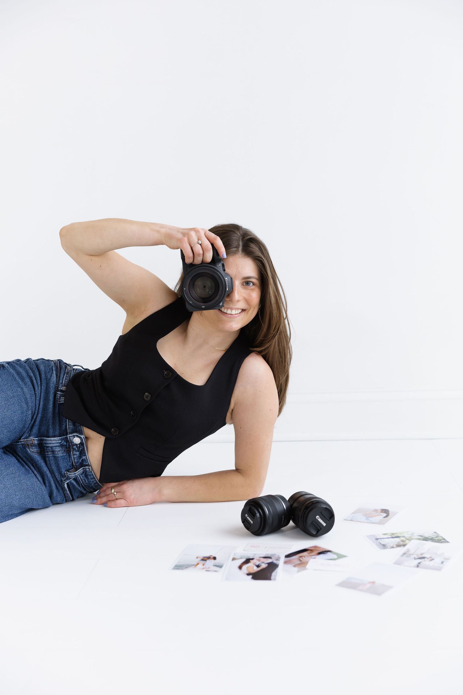 Smiling female photographer lying on floor holding camera with printed photos beside her.