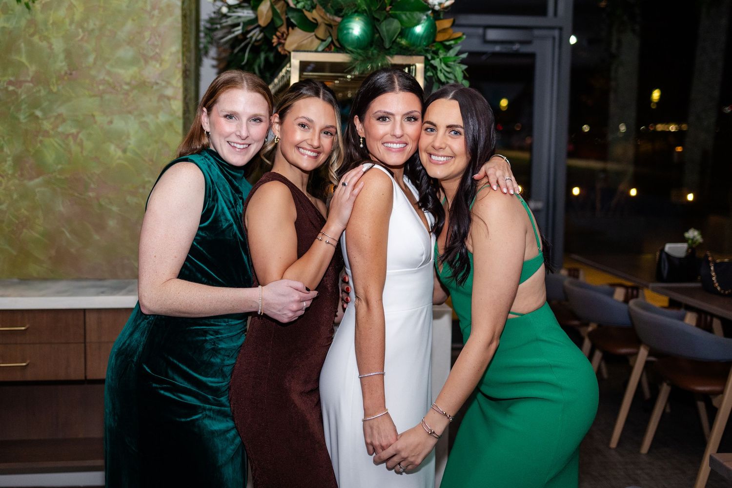 Bride posing with three bridesmaids in green and burgundy dresses at reception.