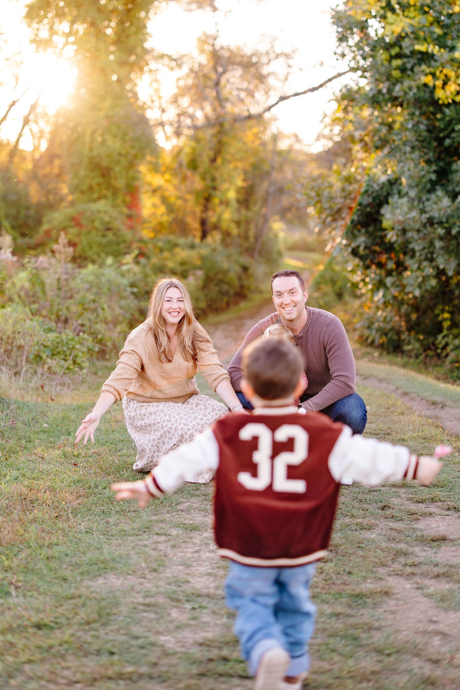 A joyful child runs toward smiling parents crouching with open arms on a sunlit autumn path.