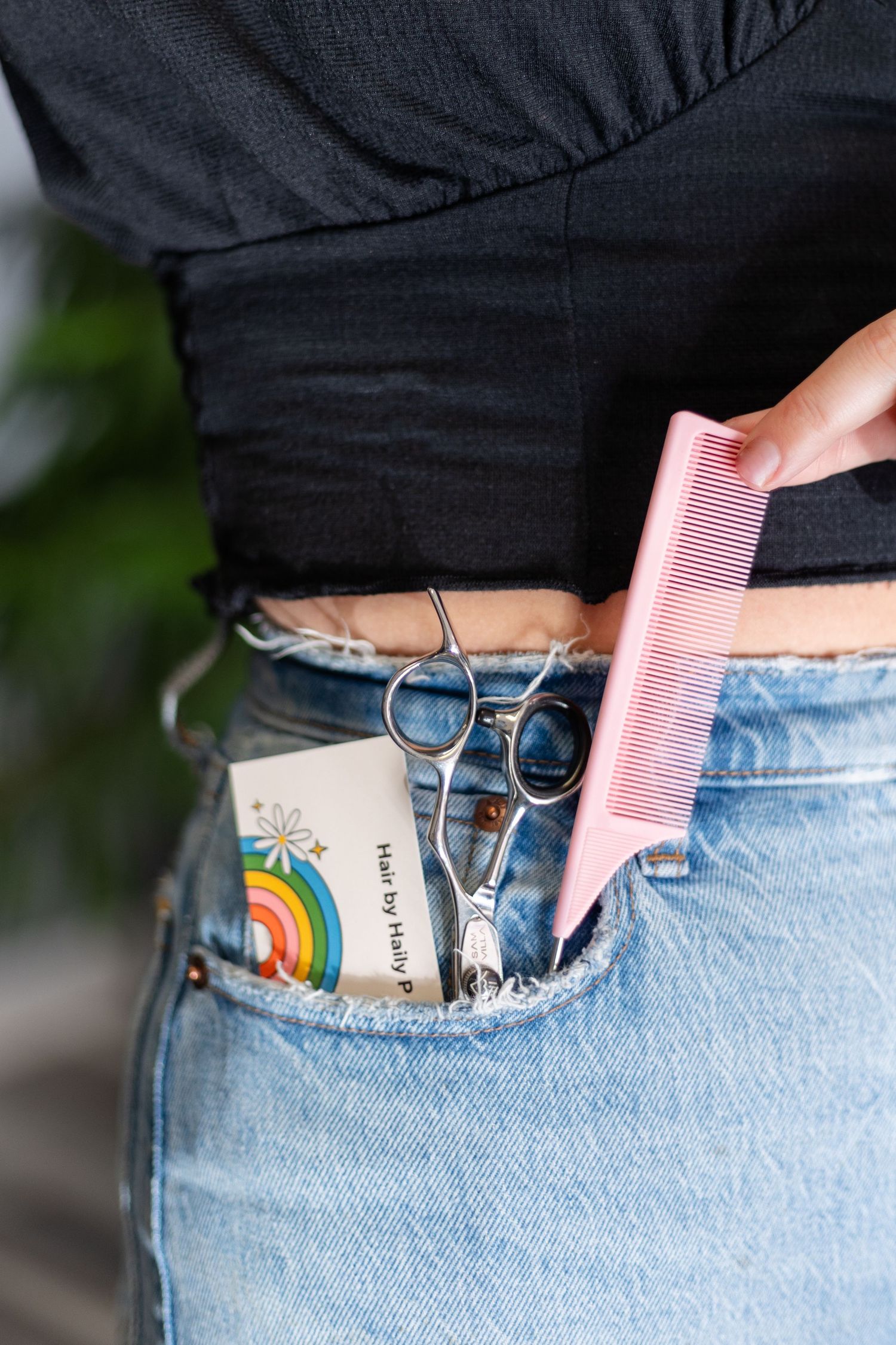 Close-up of hairstylist with scissors, comb, and business cards tucked into denim jeans pocket.