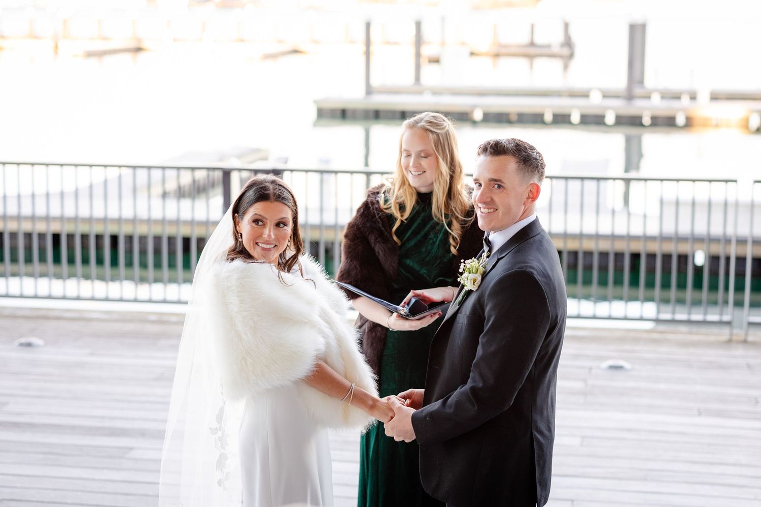 Bride and groom exchange vows with officiant at outdoor waterfront wedding ceremony.
