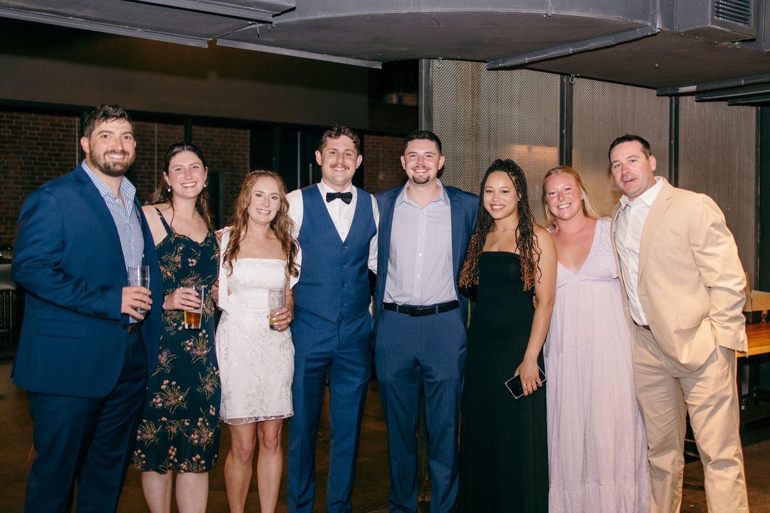 Group of seven wedding guests pose together smiling at a lively evening wedding reception celebration.