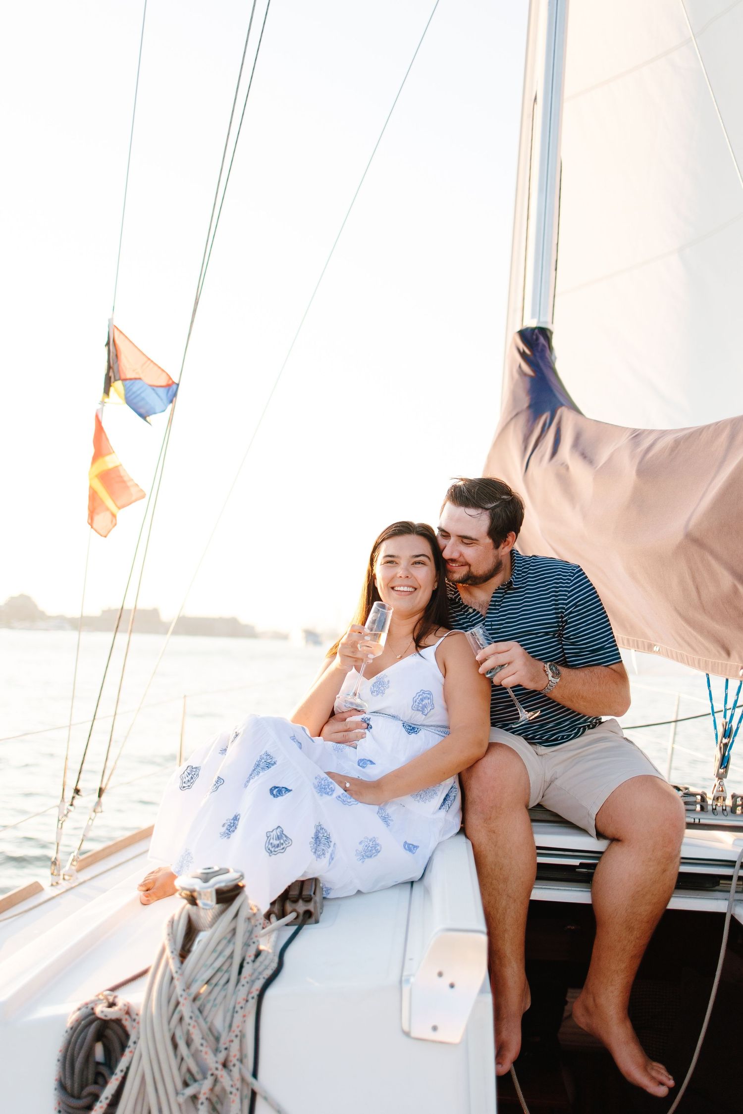 A couple relaxes on a sailboat, sharing champagne and a kiss while enjoying a sunny day on the water.