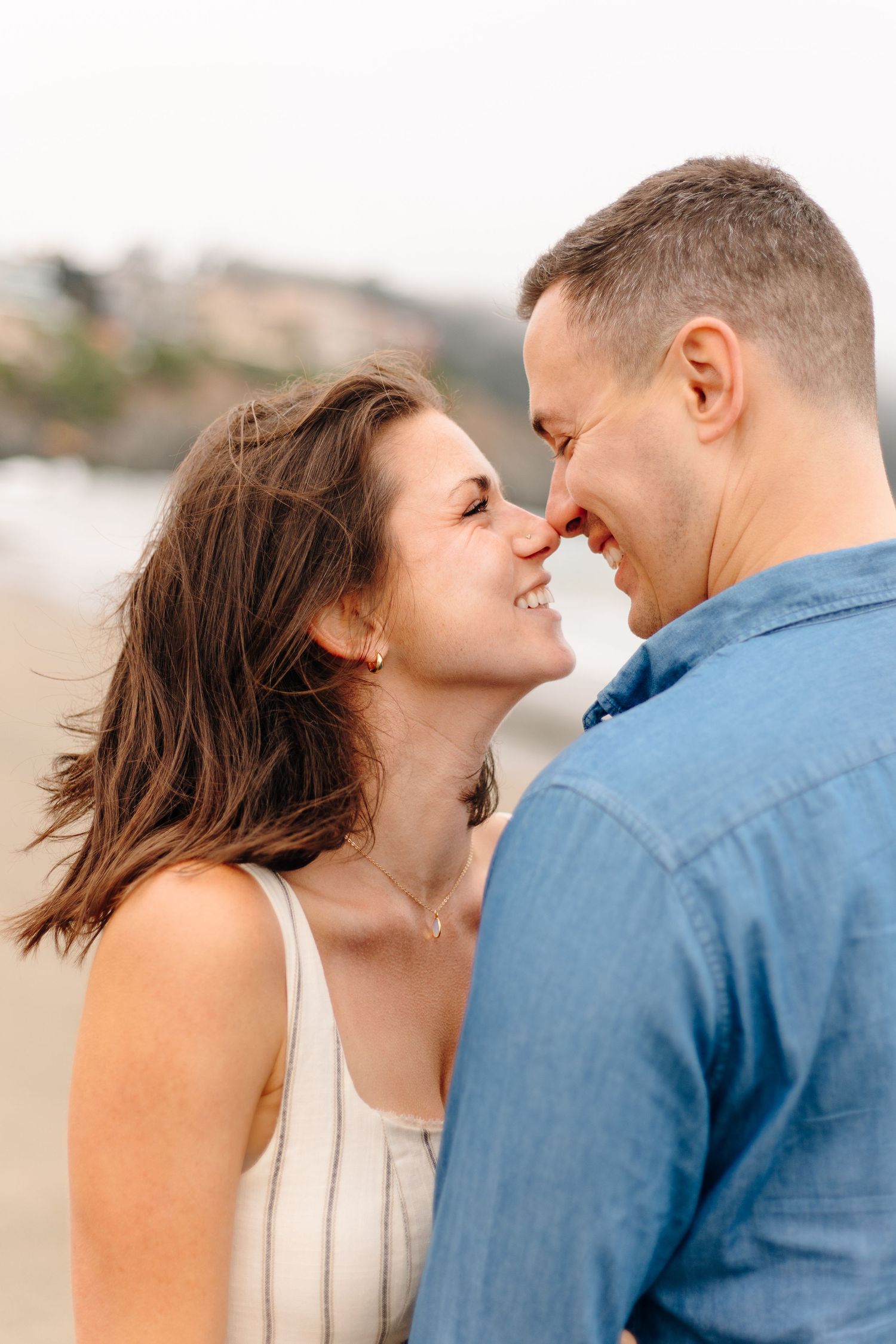 Romantic close-up of a smiling couple nearly kissing on a breezy beach.
