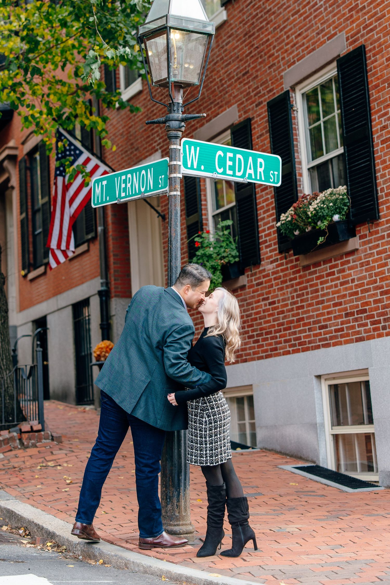A couple shares a romantic kiss beneath street signs at Mt. Vernon and W. Cedar St. in a brick city neighborhood.
