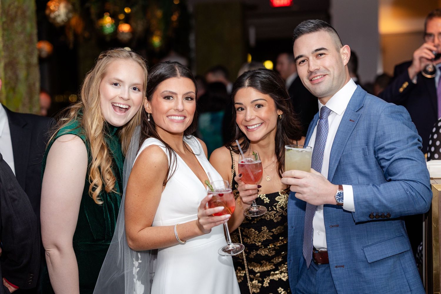 Four wedding guests smiling and holding cocktails at elegant reception venue.