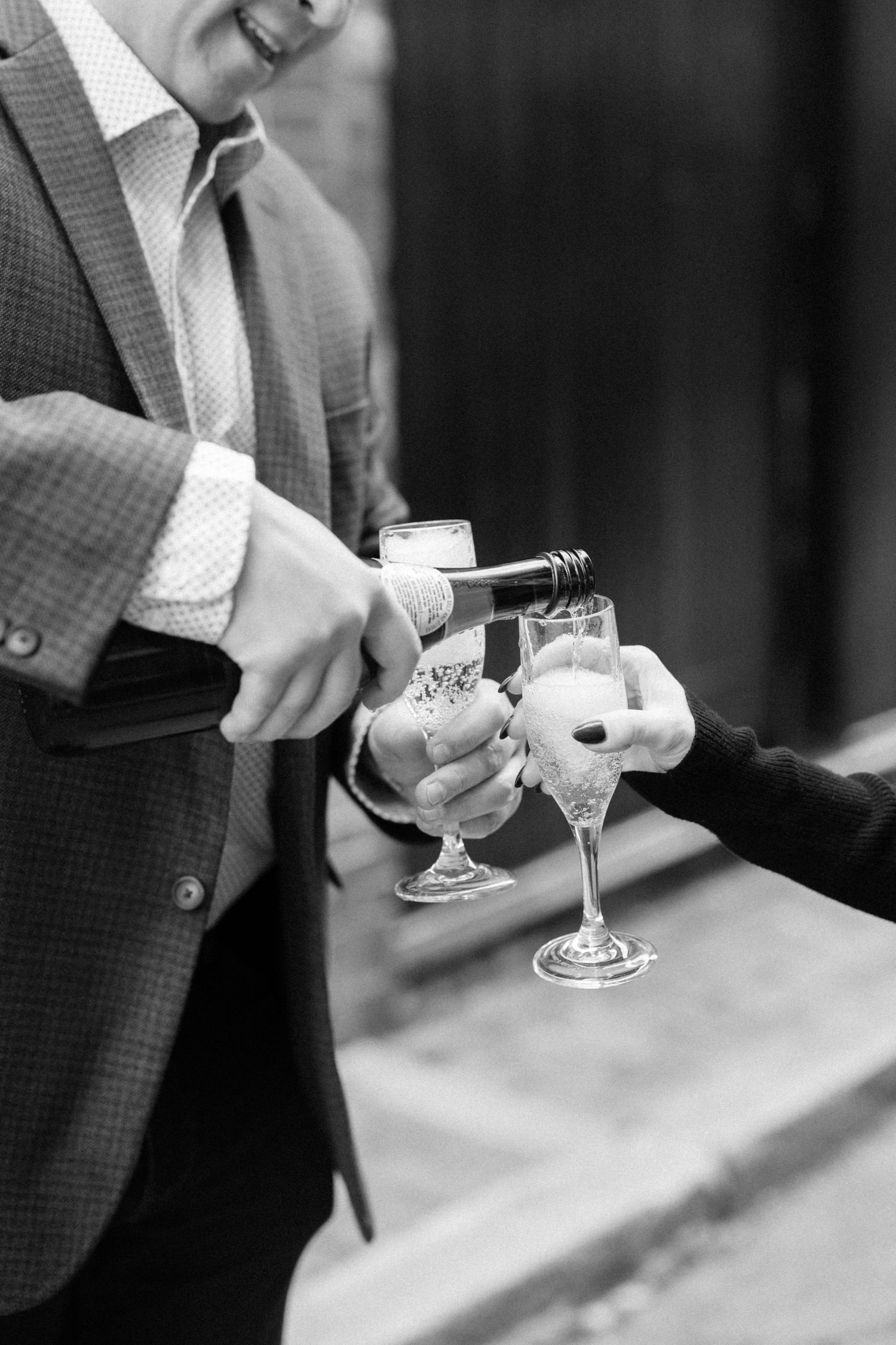 Black and white photo of man pouring champagne into glasses at a wedding celebration.