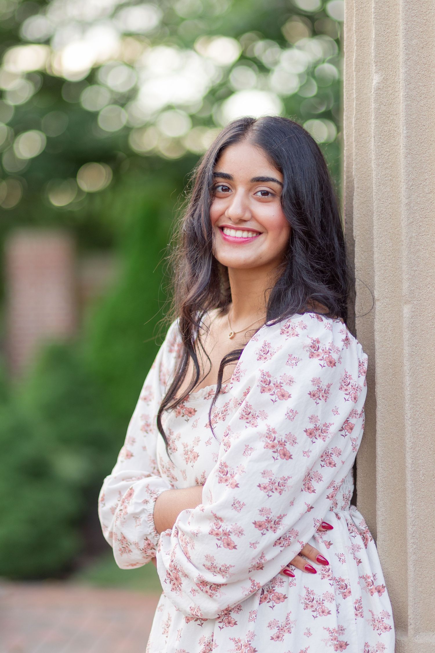 Young woman in floral dress smiling against stone column outdoors.