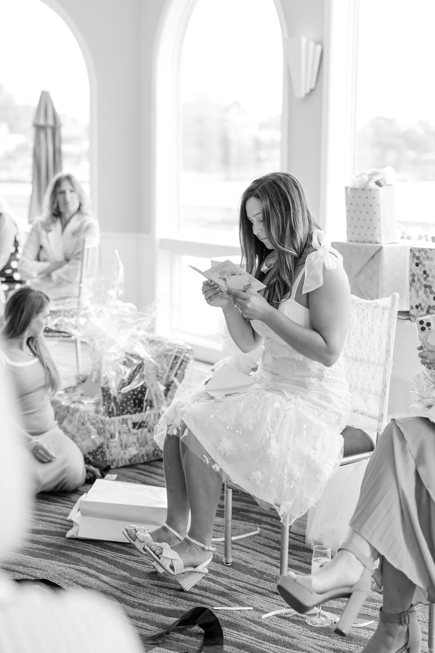 Black and white photo of a bride-to-be reading a card while opening gifts at her bridal shower.