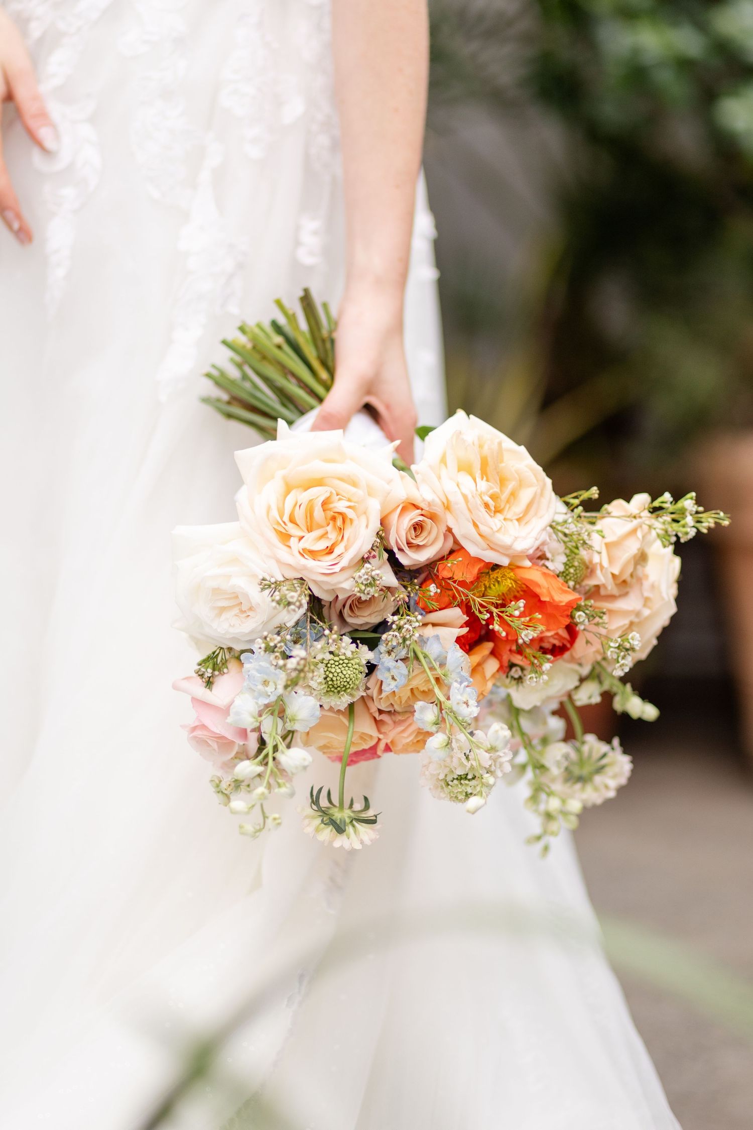 Close-up of bridal bouquet with peach roses and orange blooms in white gown.