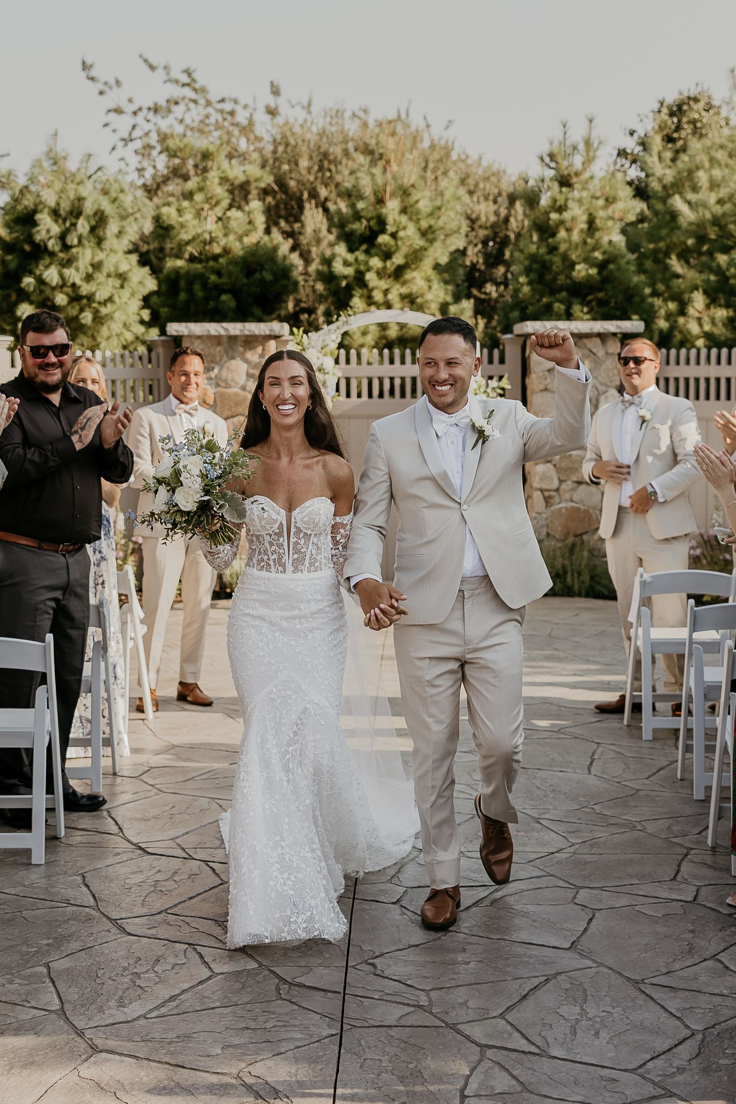 Joyful newlyweds walking down the aisle after their outdoor wedding ceremony surrounded by guests.