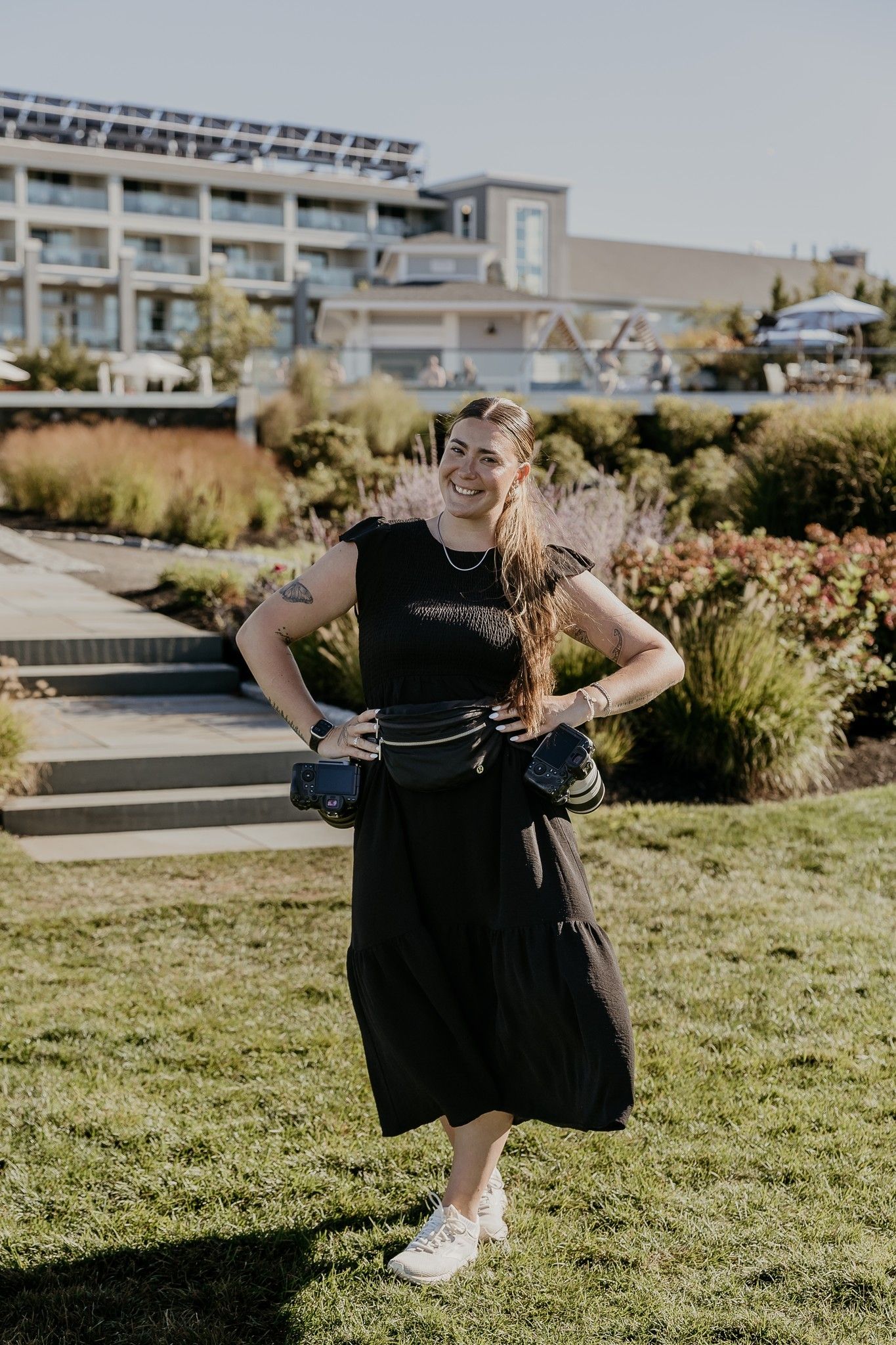 Smiling female wedding photographer in a black outfit posing outdoors at a resort venue.