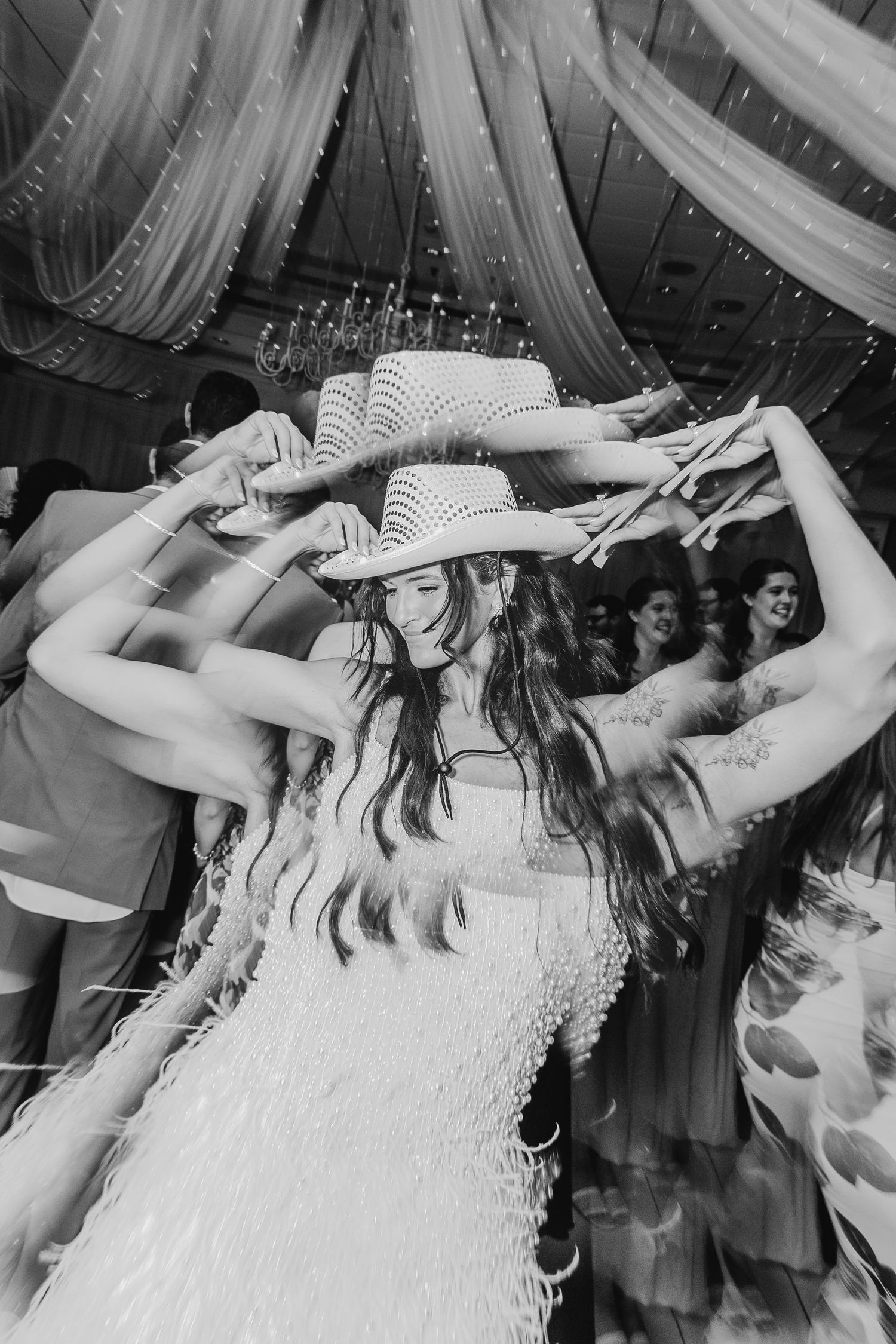 Black and white photo of a bride dancing joyfully in a cowboy hat and fringe dress at her wedding reception.