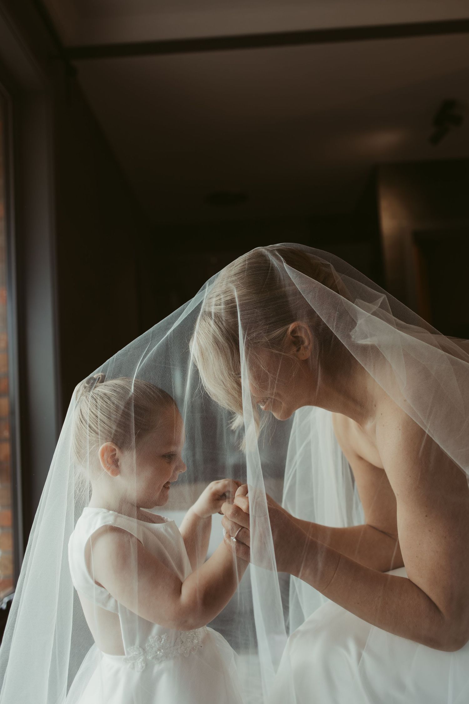 Bride sharing a tender moment with young flower girl under wedding veil.