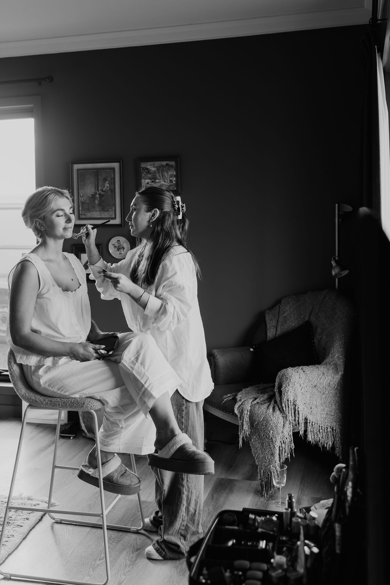 Black and white photo of bride having makeup applied by artist in moody wedding preparation room.