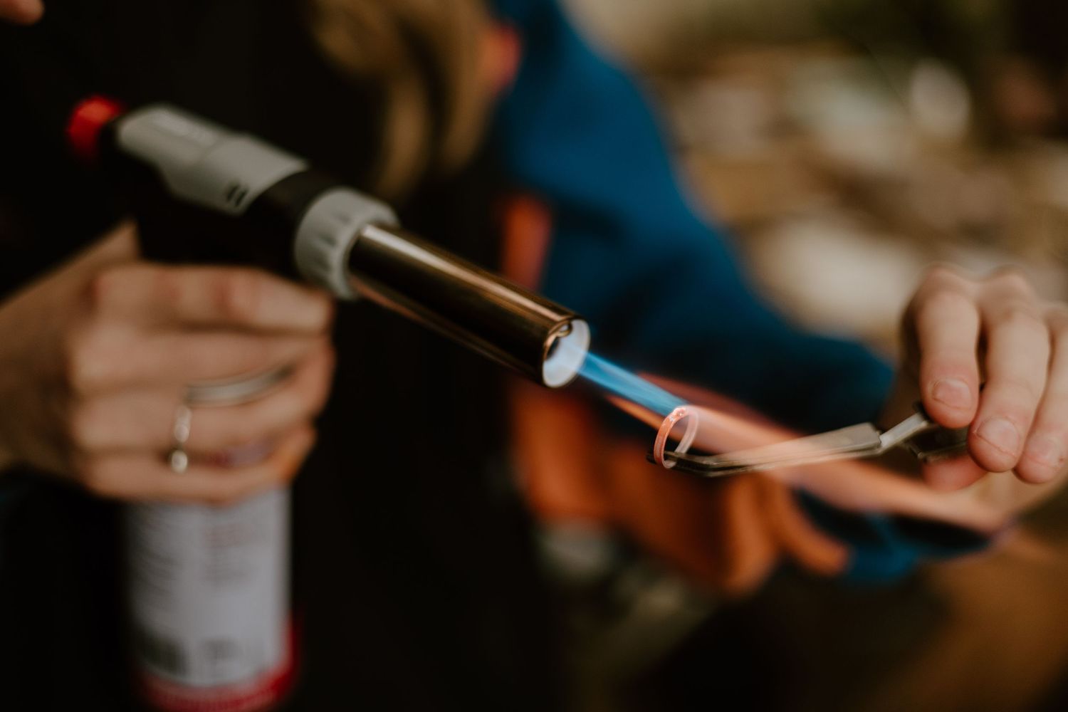 Close-up of hands using a butane torch to heat a copper pipe fitting during a soldering or plumbing repair task.