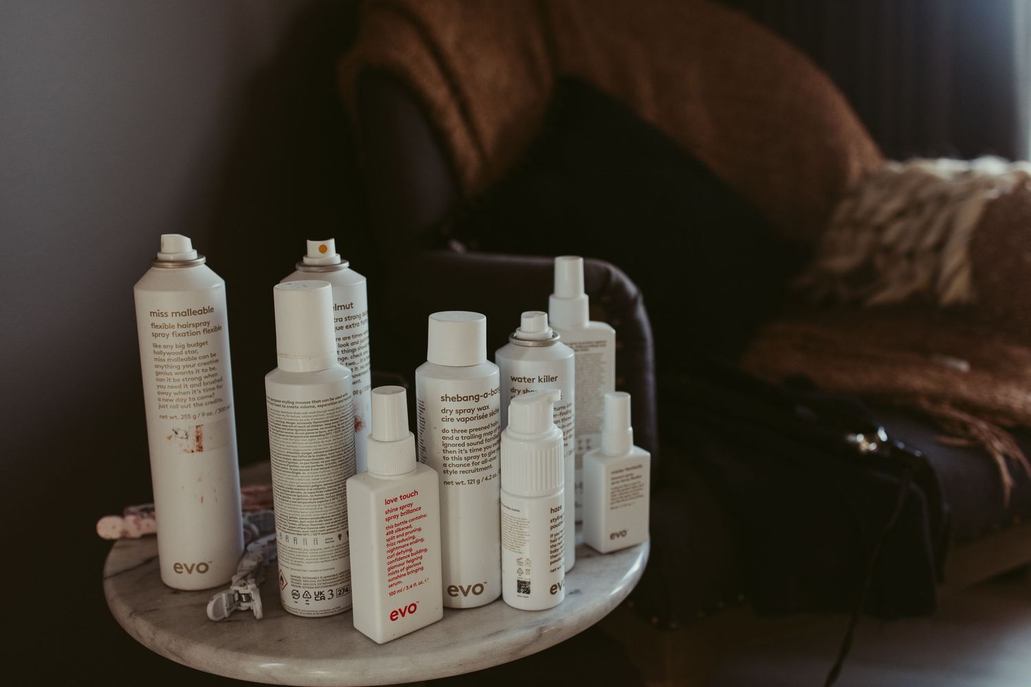 A collection of EVO hair care products arranged on a small round table beside a leather couch.
