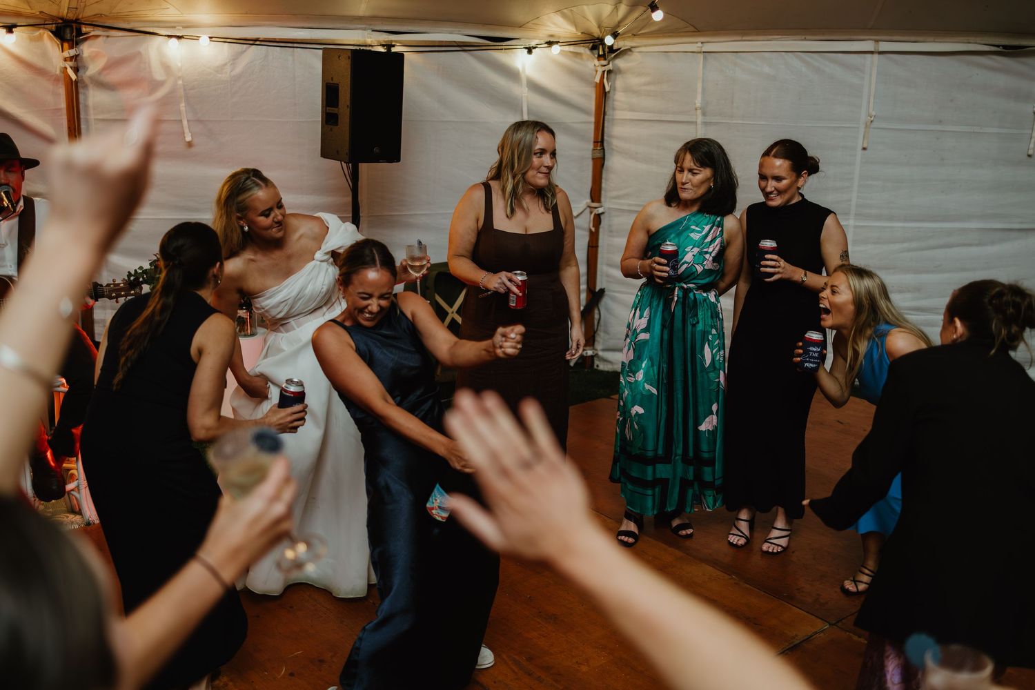 Bride dancing energetically with guests on crowded wedding reception dance floor under tent.