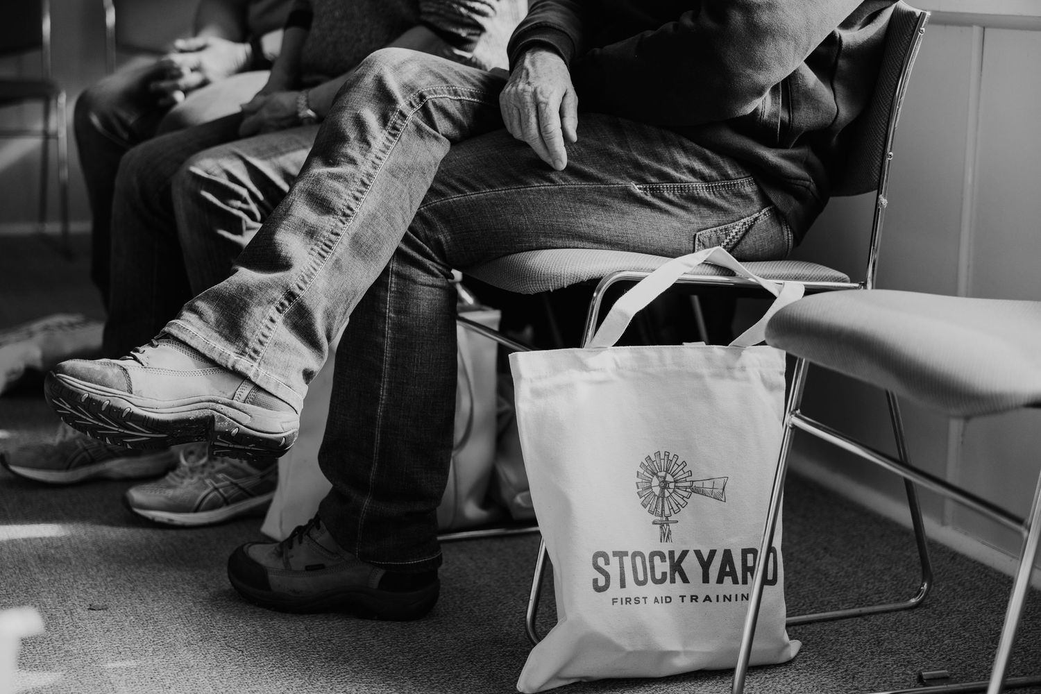 People sitting with a Stockyard tote bag on the floor in a black and white photo.