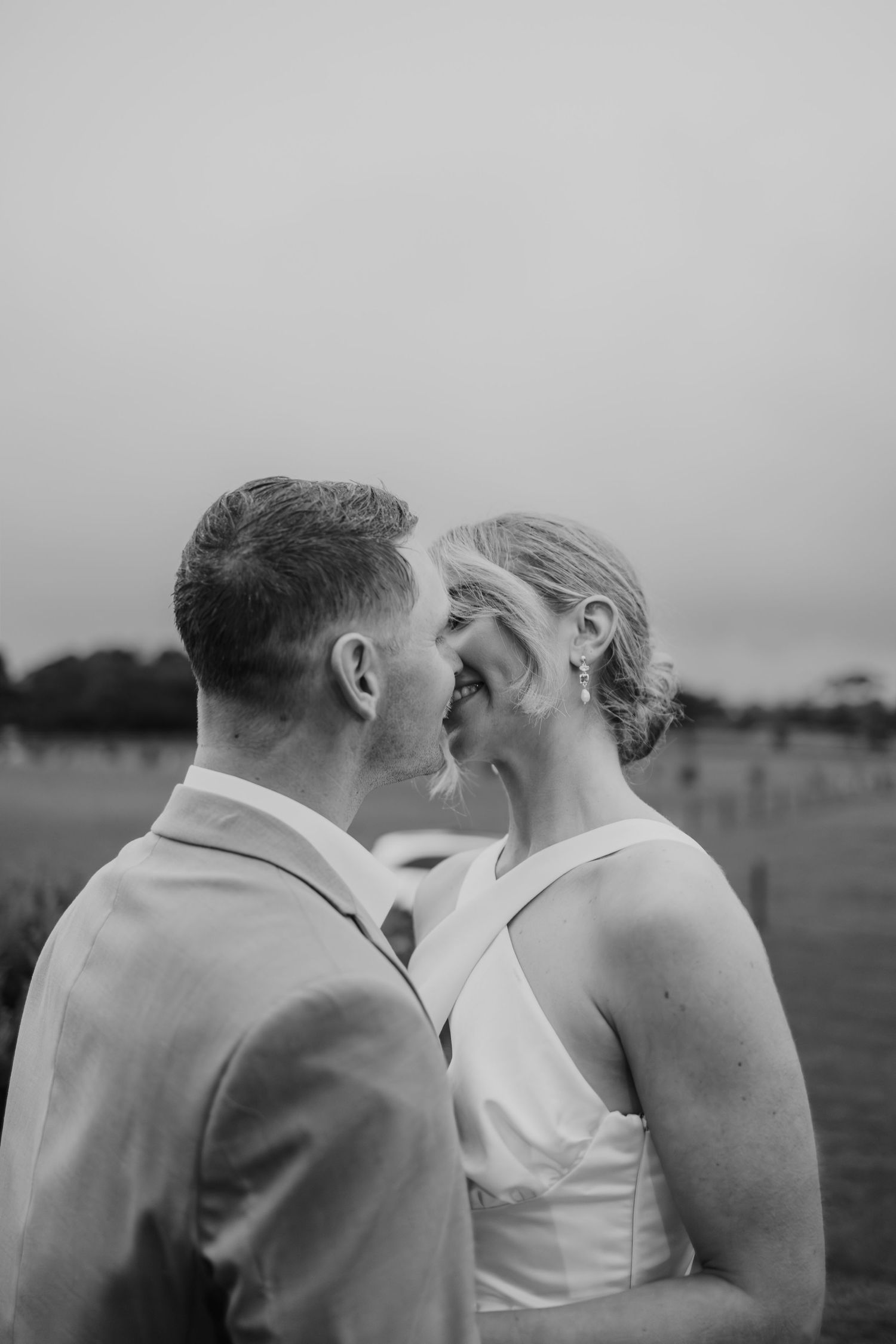 Black and white romantic moment of bride and groom almost kissing in open field at dusk.