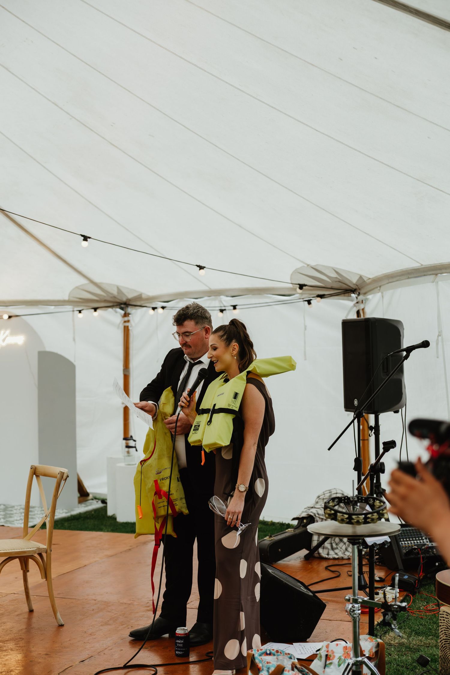 Wedding entertainer performing a magic trick with a guest in a marquee reception tent with string lights.