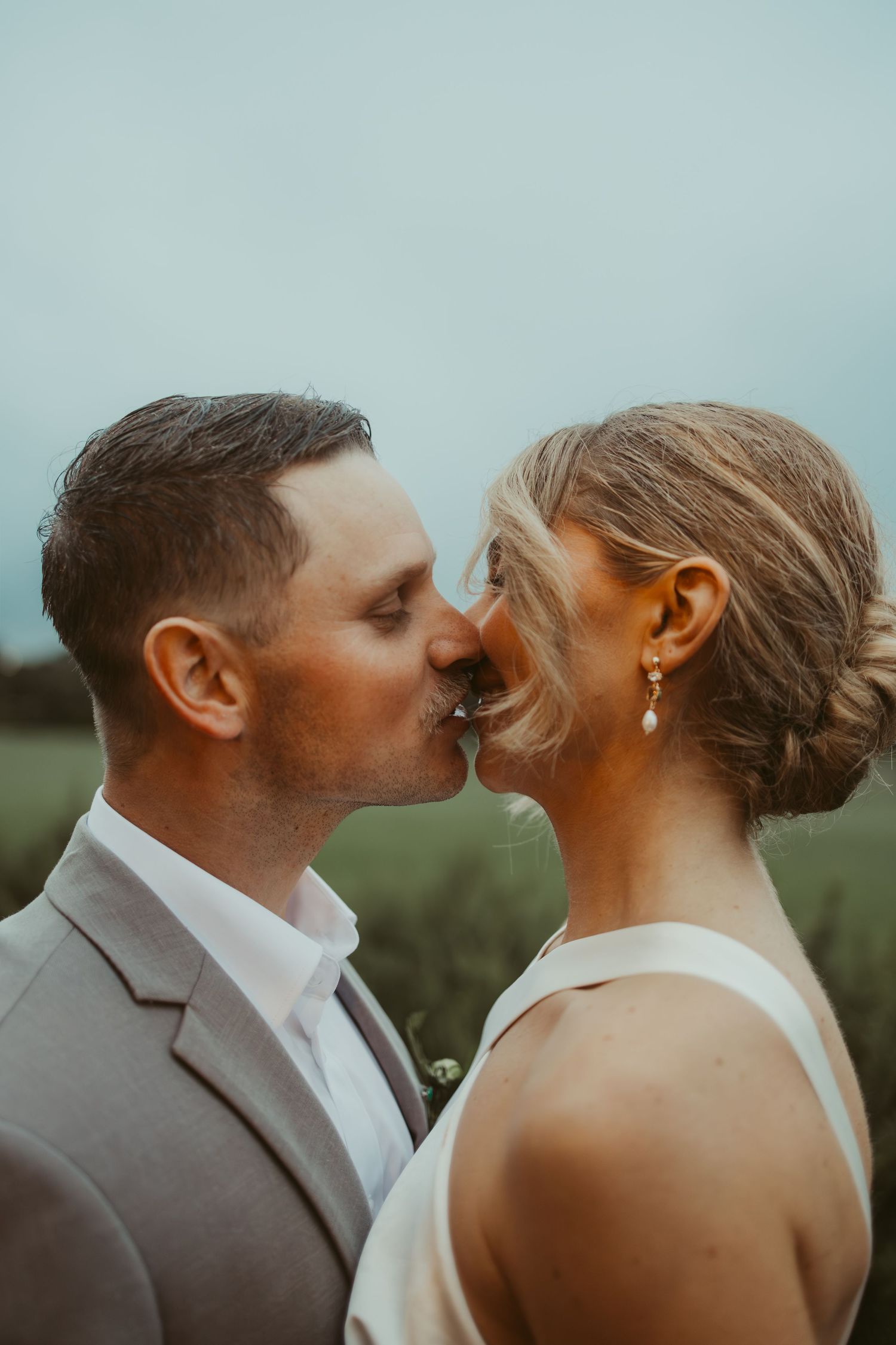 Bride and groom sharing a romantic kiss outdoors with a soft green field background.
