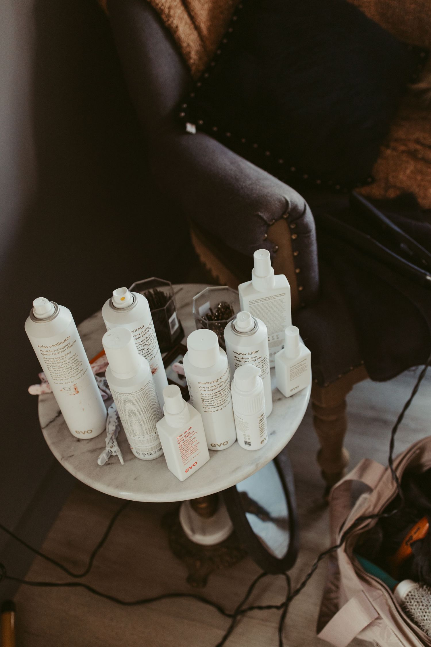 Assortment of white hair and beauty product bottles arranged on a small round table for bridal preparation.