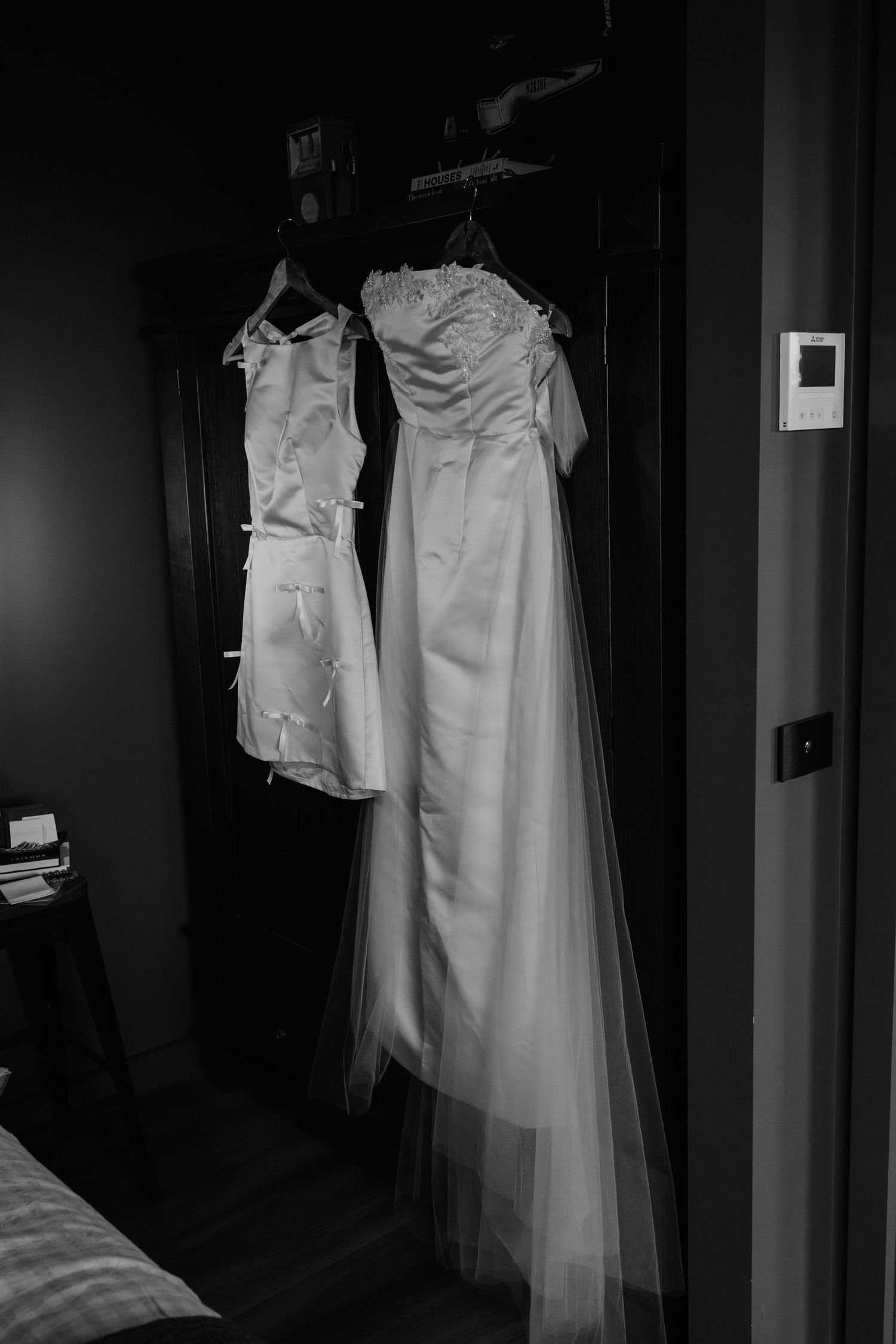 Black and white photo of two wedding dresses hanging on a dark door before the ceremony.
