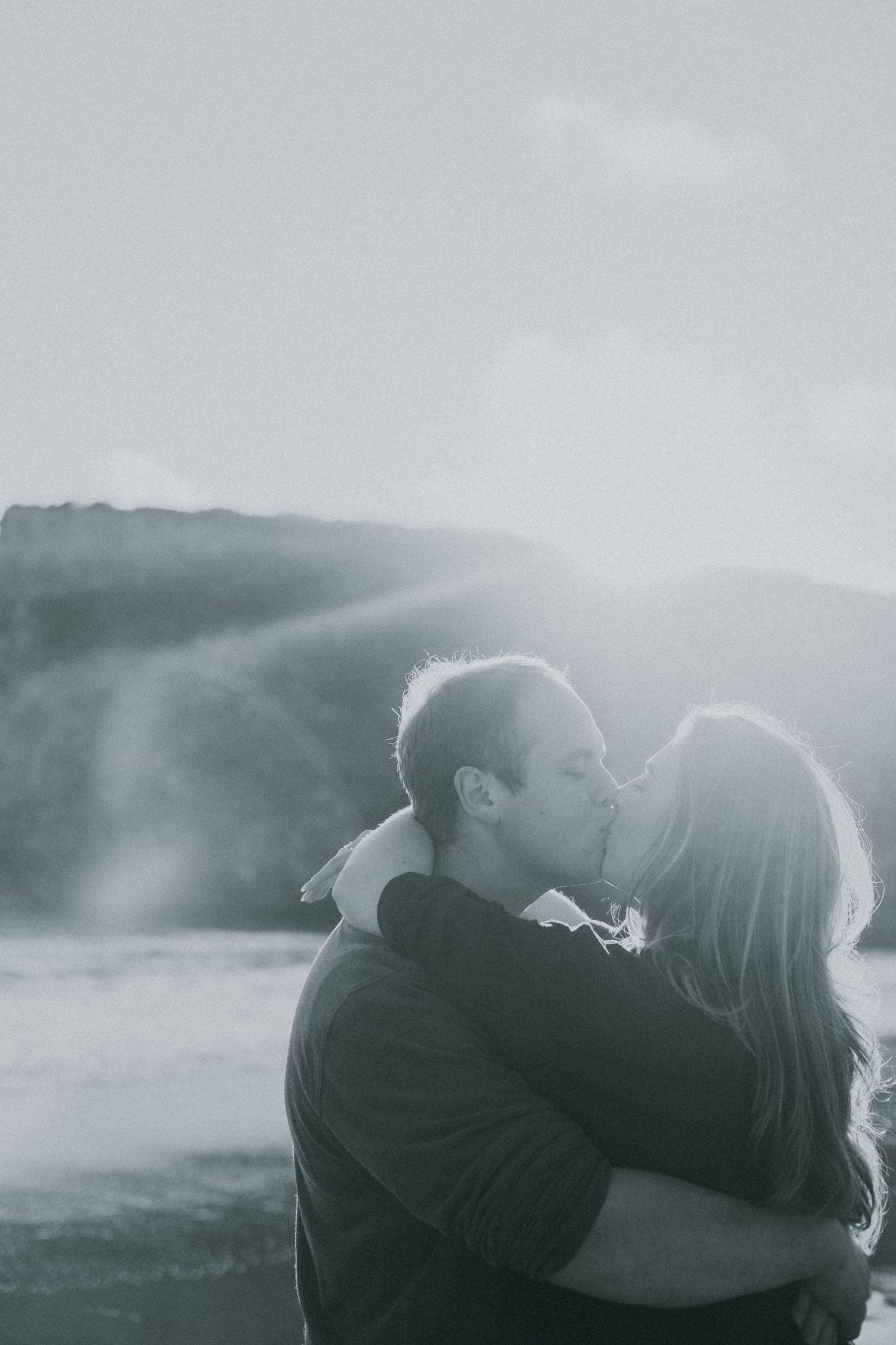 A couple shares a romantic kiss on a beach in a dreamy black and white photo.