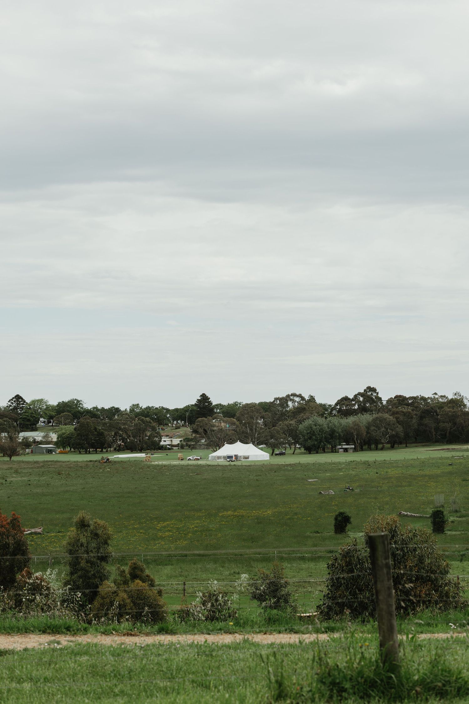 Lush green farmland with a white marquee tent and trees under an overcast sky.