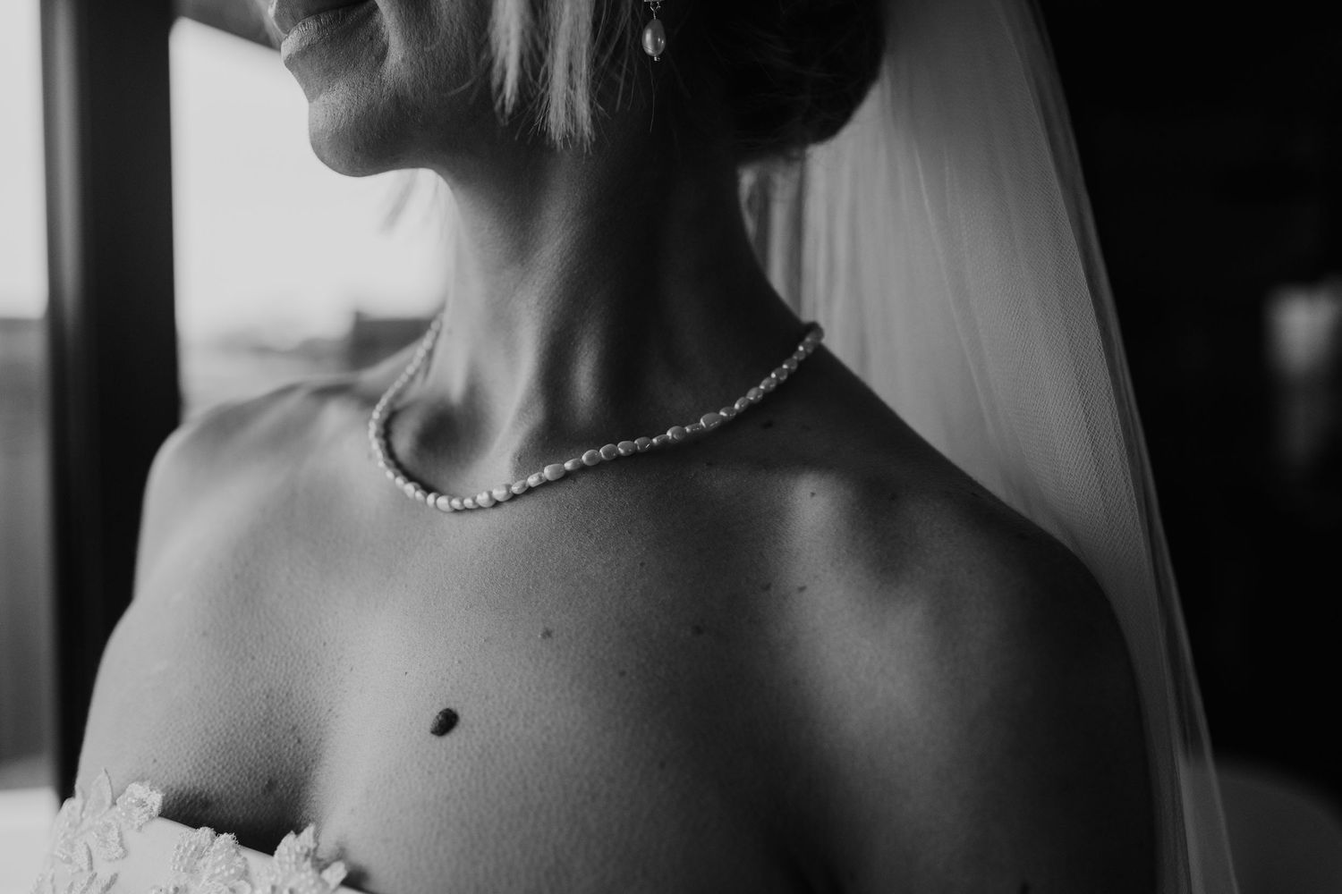Black and white close-up of bride wearing pearl necklace and veil with elegant bare shoulder detail.
