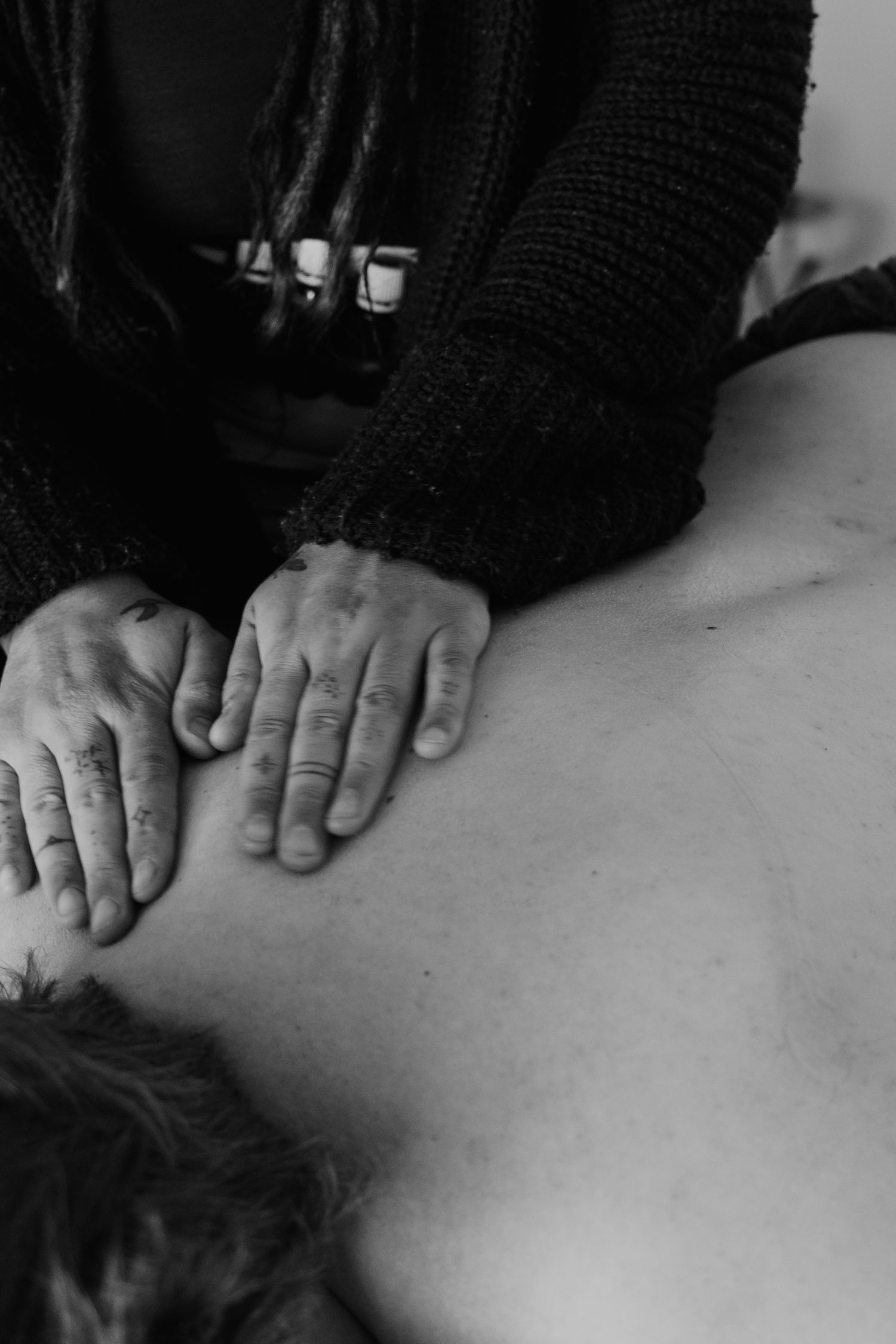 Black and white photo of a massage therapist pressing hands firmly on a client's bare back during a therapeutic session.