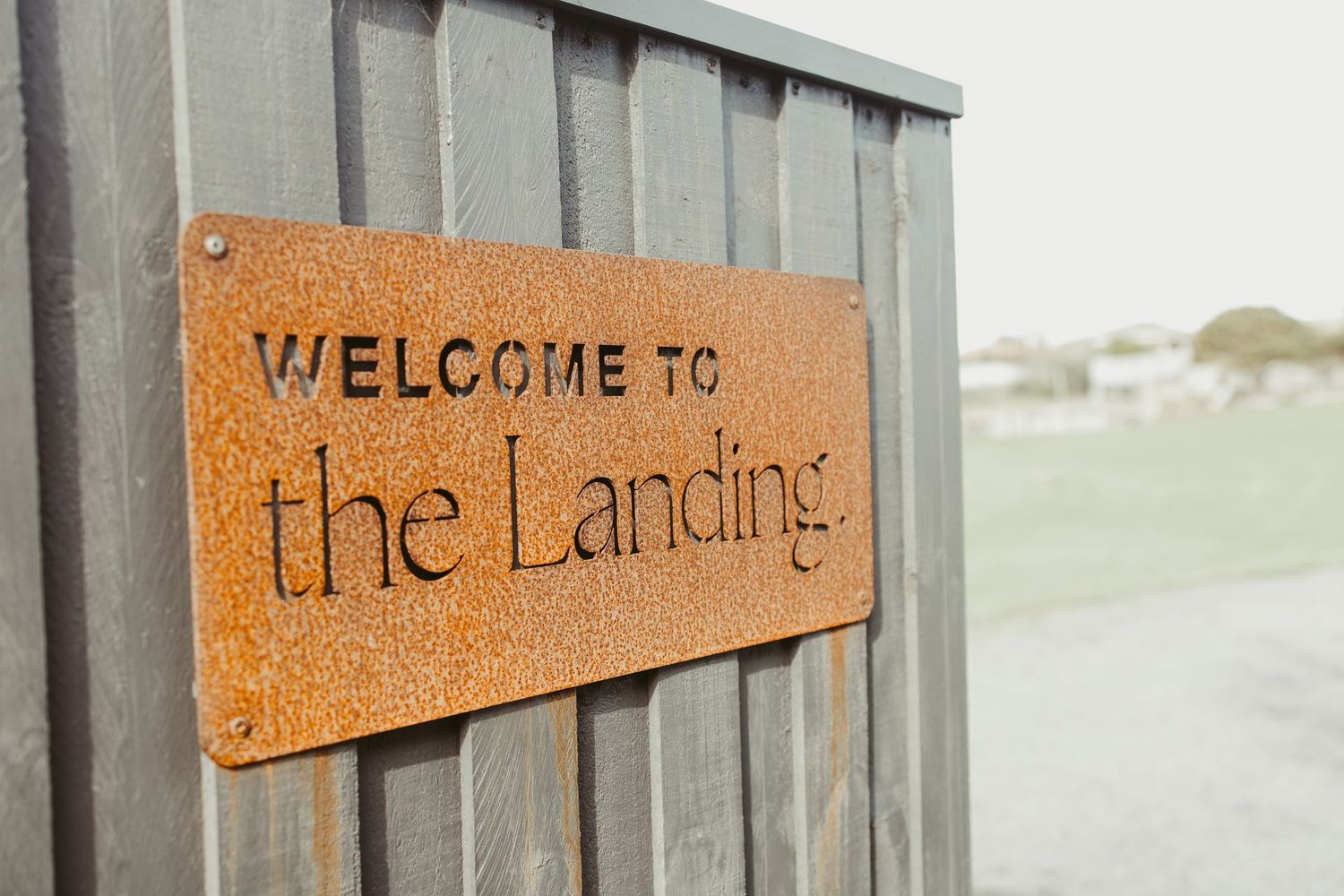 Rustic weathered metal welcome sign reading Welcome to The Landing mounted on wooden fence.