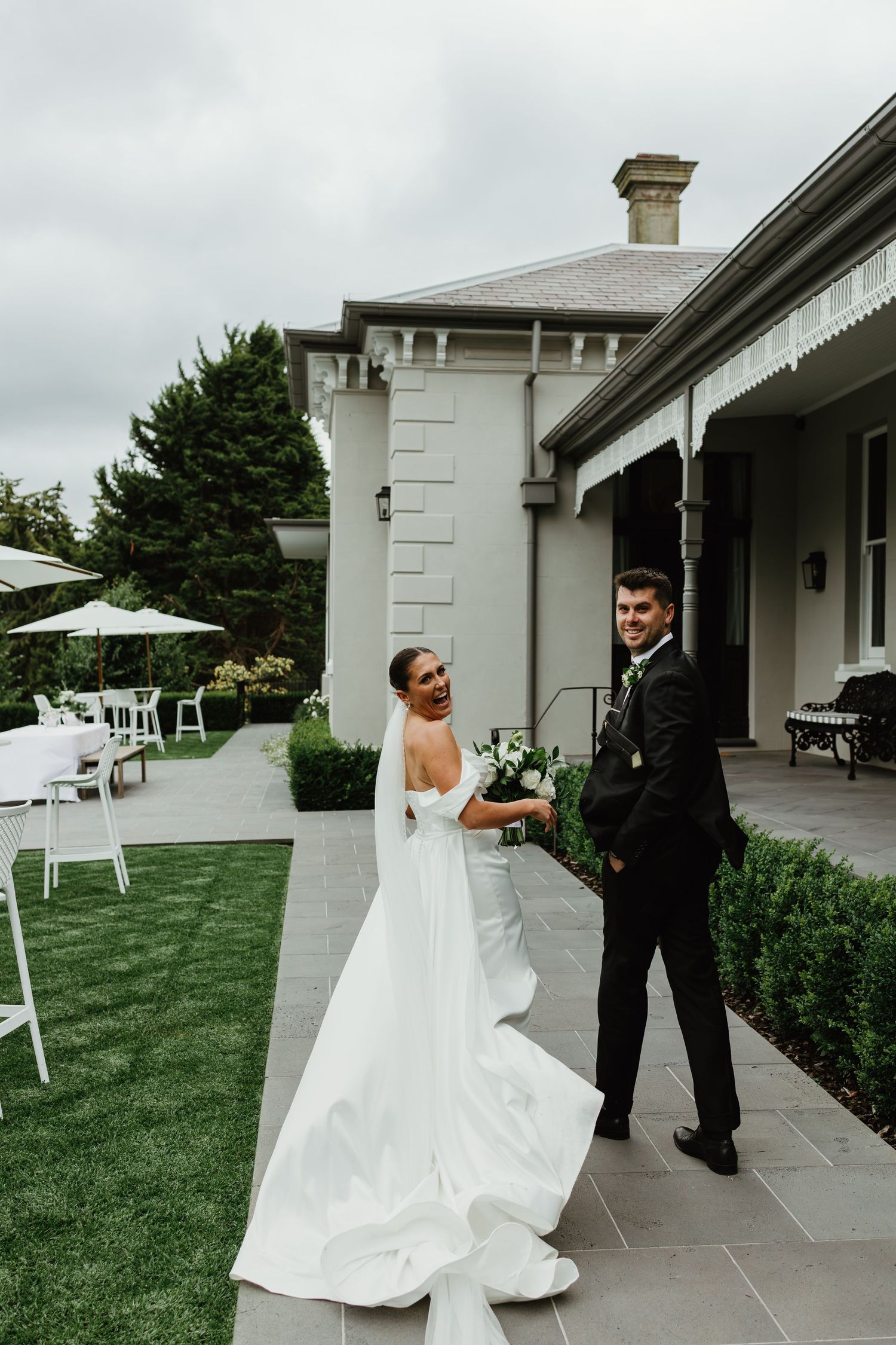 Smiling bride and groom pose together on a patio outside an elegant grey estate wedding venue.