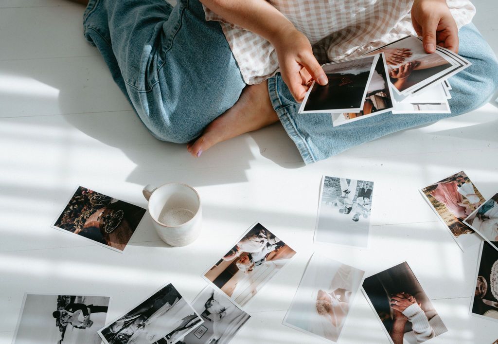 Overhead view of person sitting cross-legged on white floor surrounded by printed photographs and a white mug.