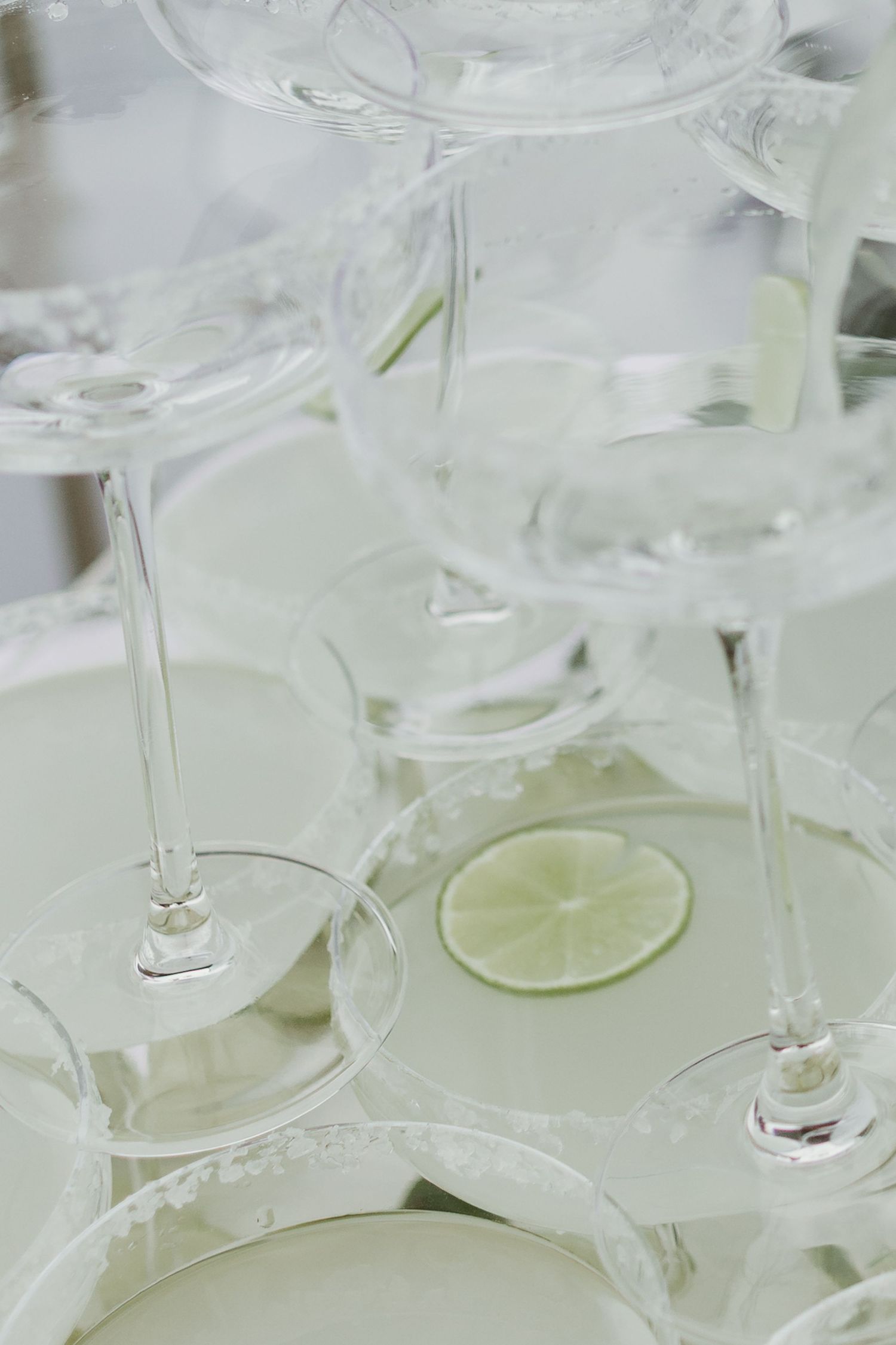 Elegant pyramid of coupe champagne glasses with salted rims and lime slices for a wedding cocktail tower display.