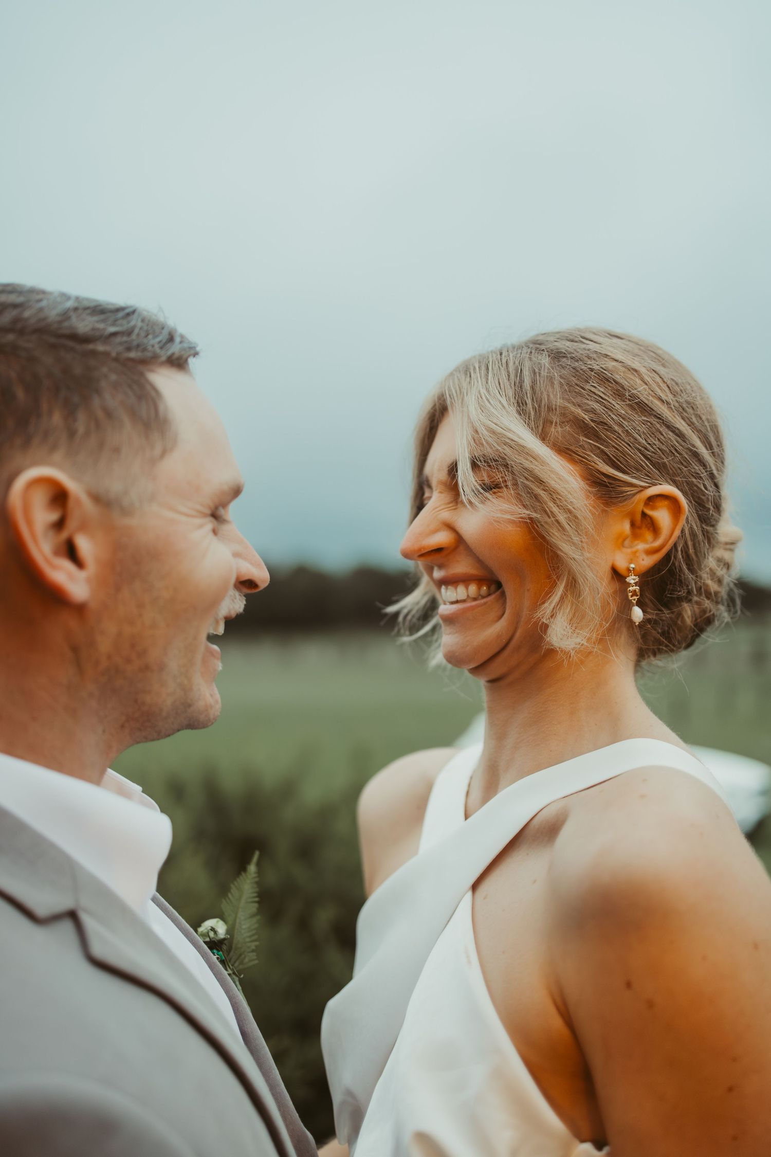 A joyful bride and groom share a loving glance while standing in a lush green field.