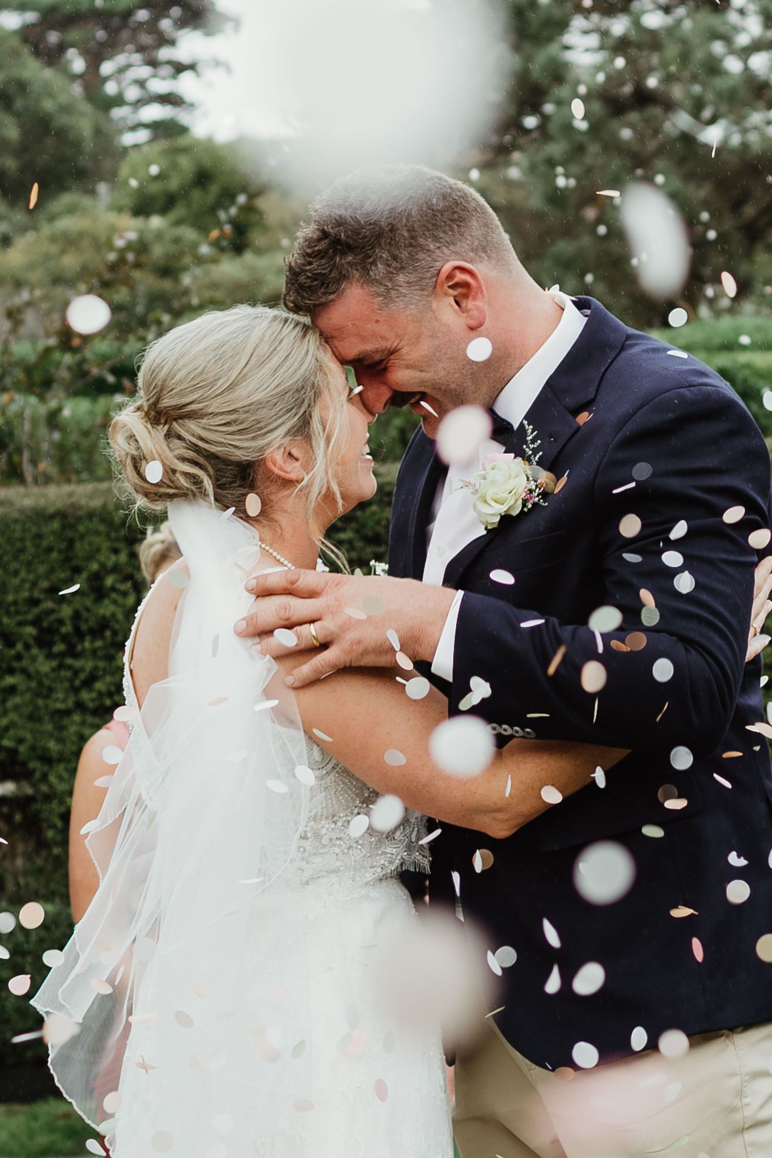 Newlywed couple sharing an intimate moment surrounded by colorful confetti in a lush garden wedding celebration.
