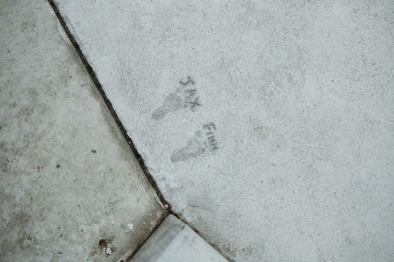 Two wet footprints imprinted on a light gray concrete floor near a diagonal crack.
