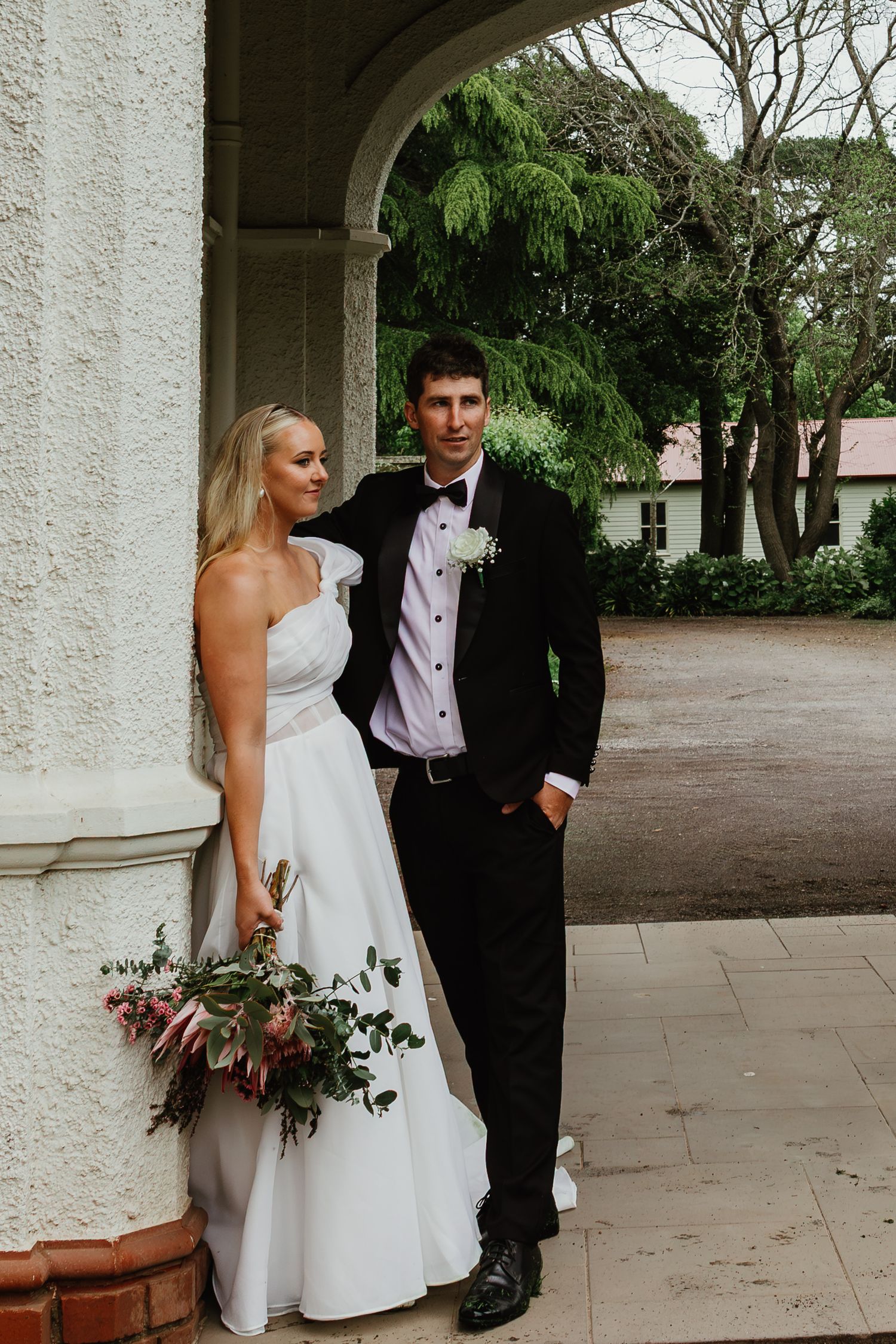 Bride and groom pose elegantly under stone arch at historic wedding venue.