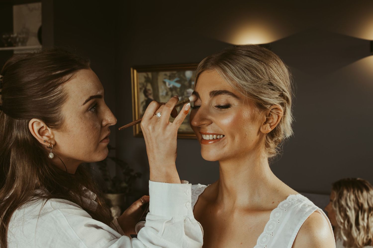 Makeup artist applying foundation to a smiling bride during wedding preparations.