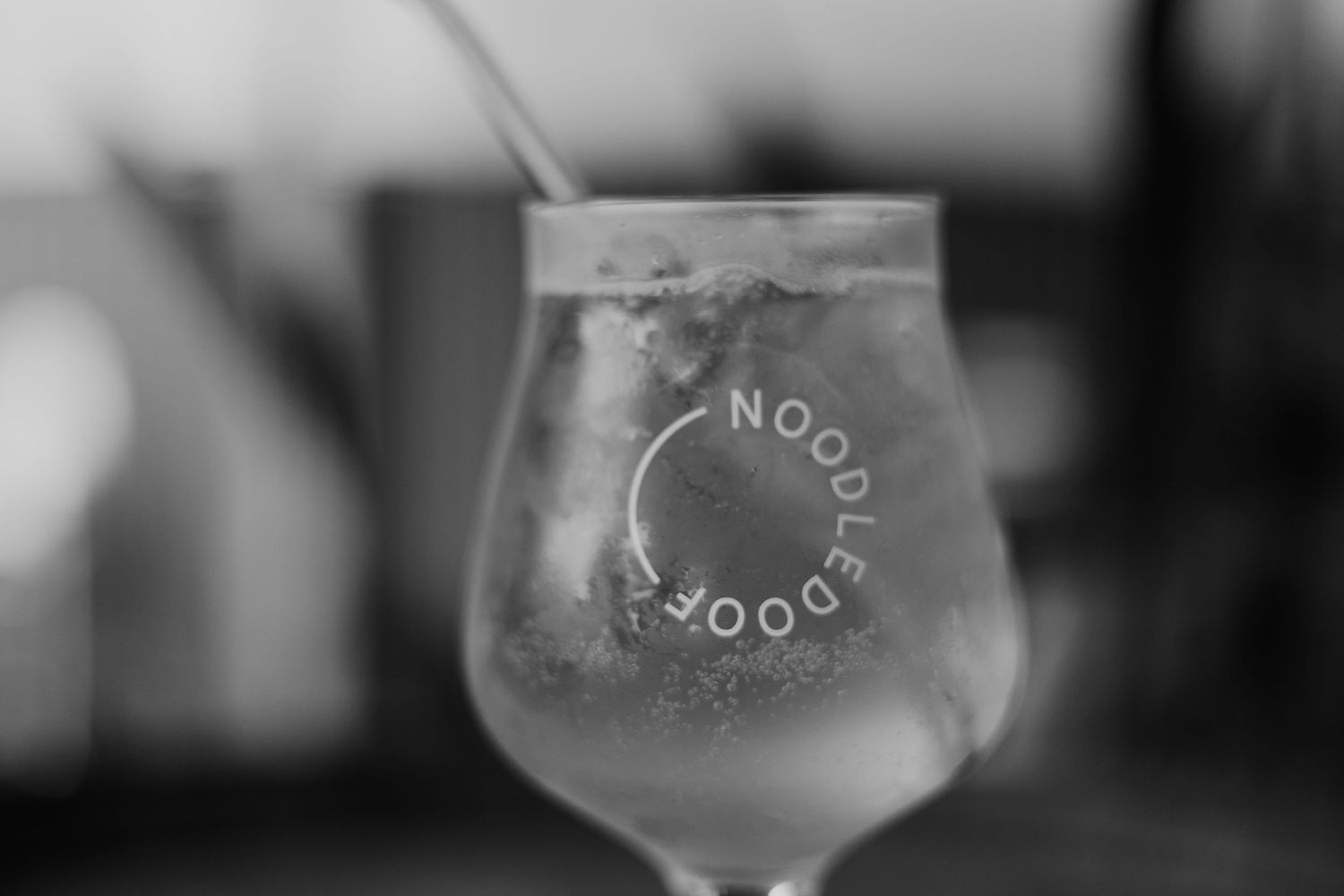 A Noodledoor branded stemmed glass with ice and a straw in black and white.