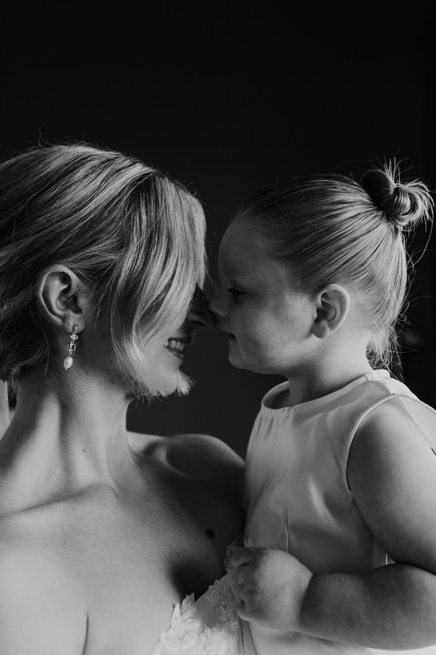 Black and white portrait of a bride smiling face to face with a young flower girl.