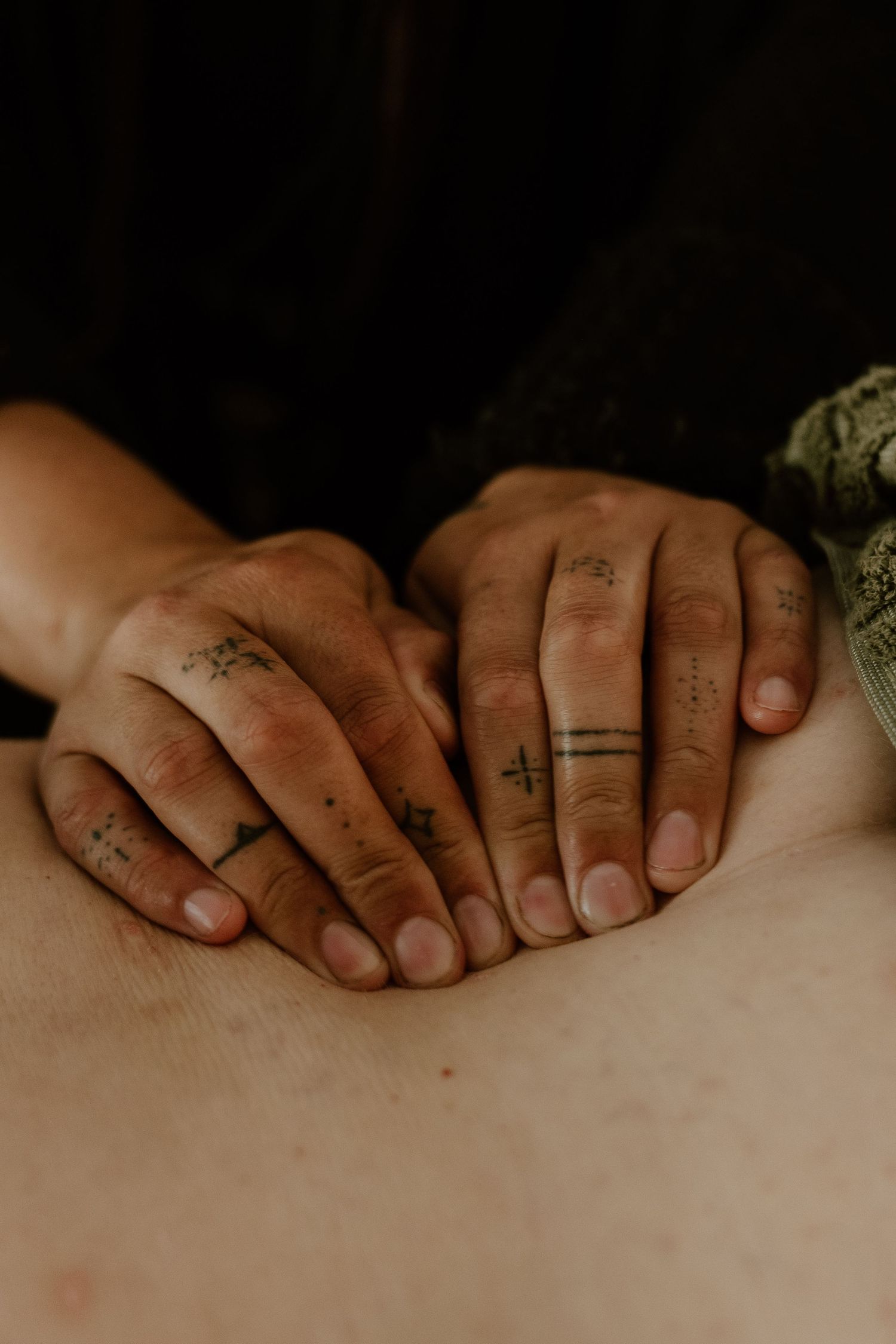 Tattooed hands with small geometric ink designs resting on a person's back during a massage therapy session.