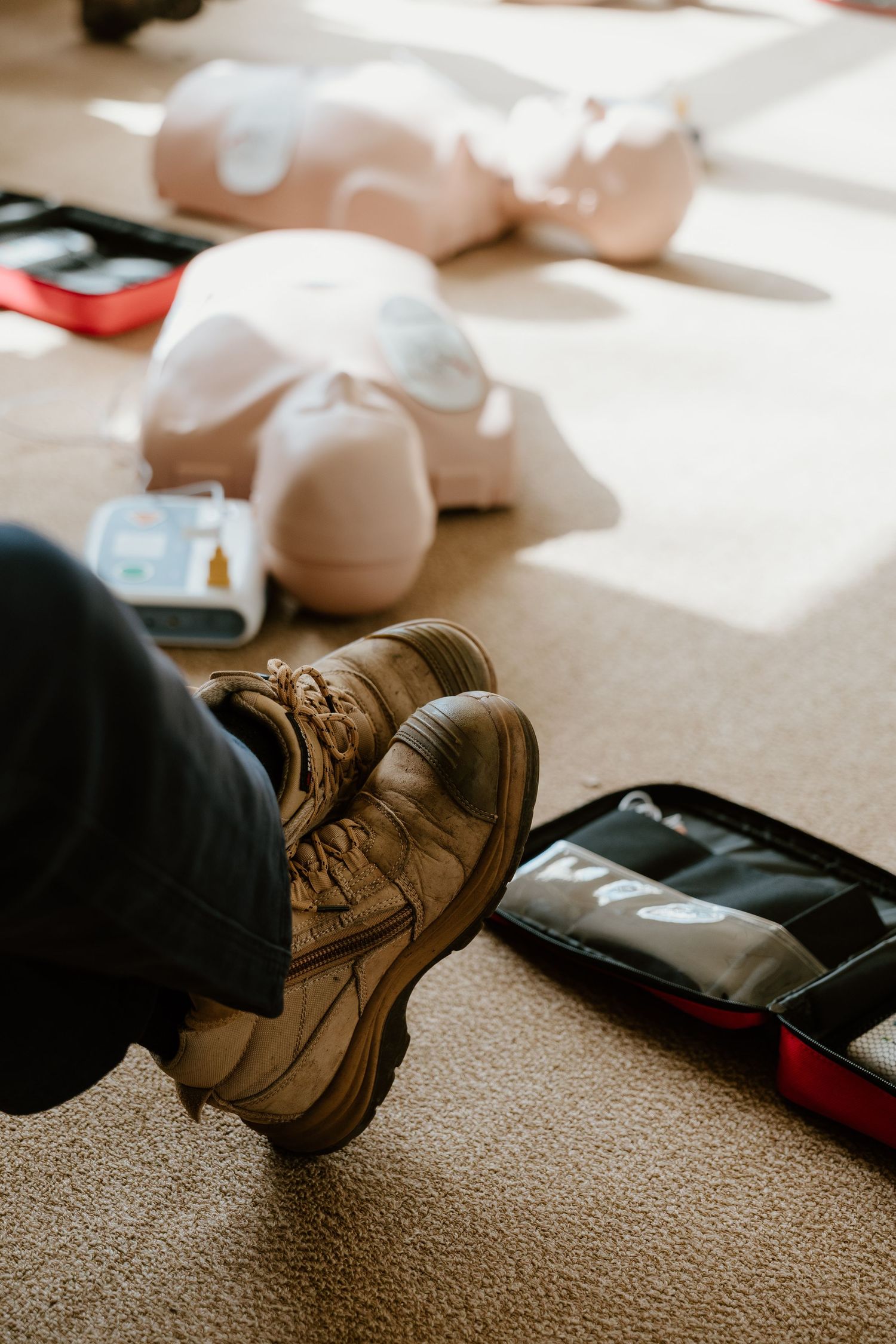 CPR training mannequins and first aid kit on carpet floor during emergency response training course.