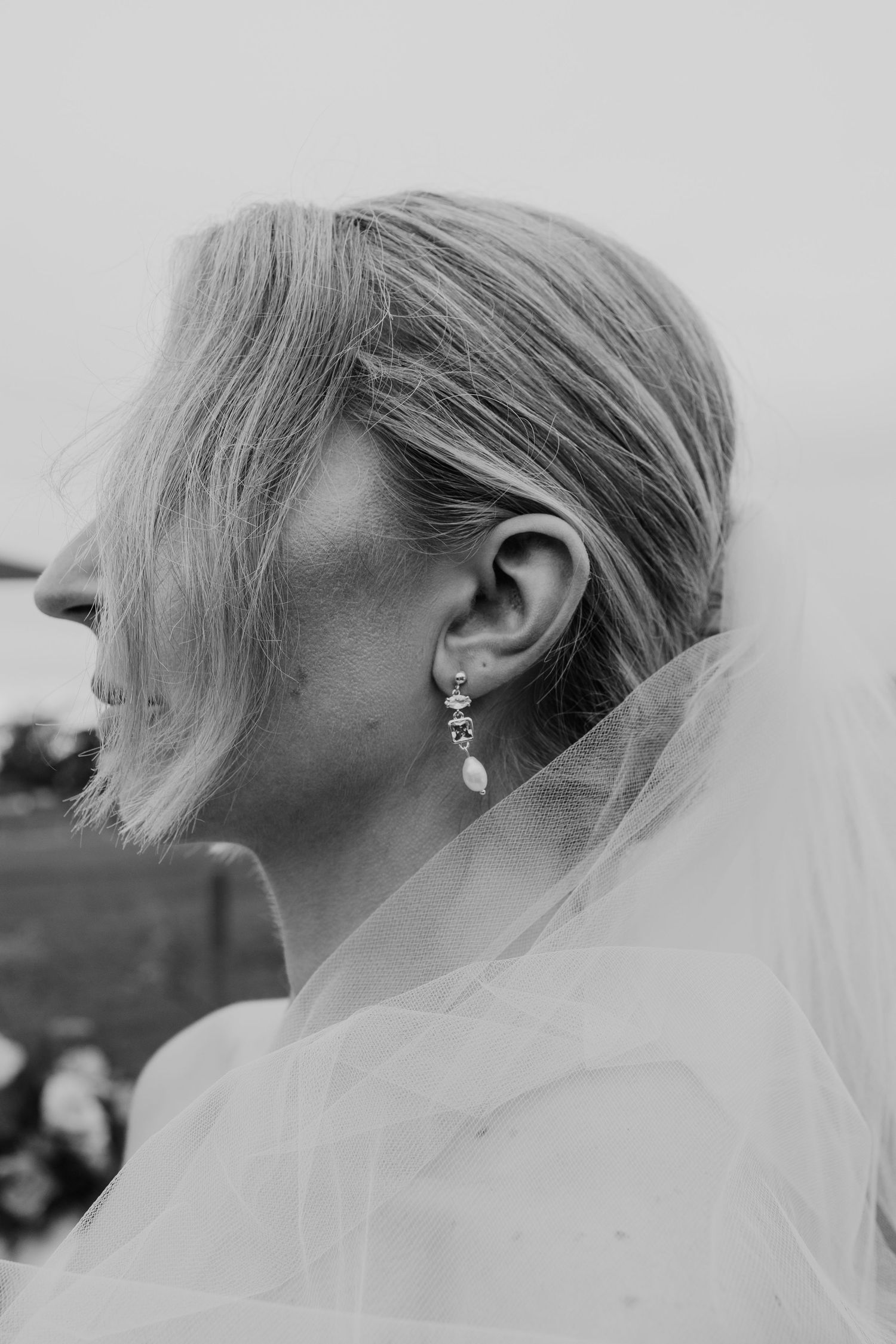 Black and white profile portrait of a bride wearing a delicate drop earring with veil draped over shoulder.