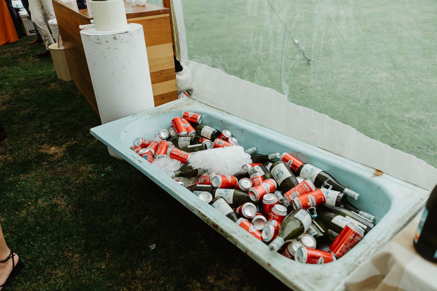 Vintage bathtub filled with ice, Coca-Cola cans and beer bottles at an outdoor wedding.